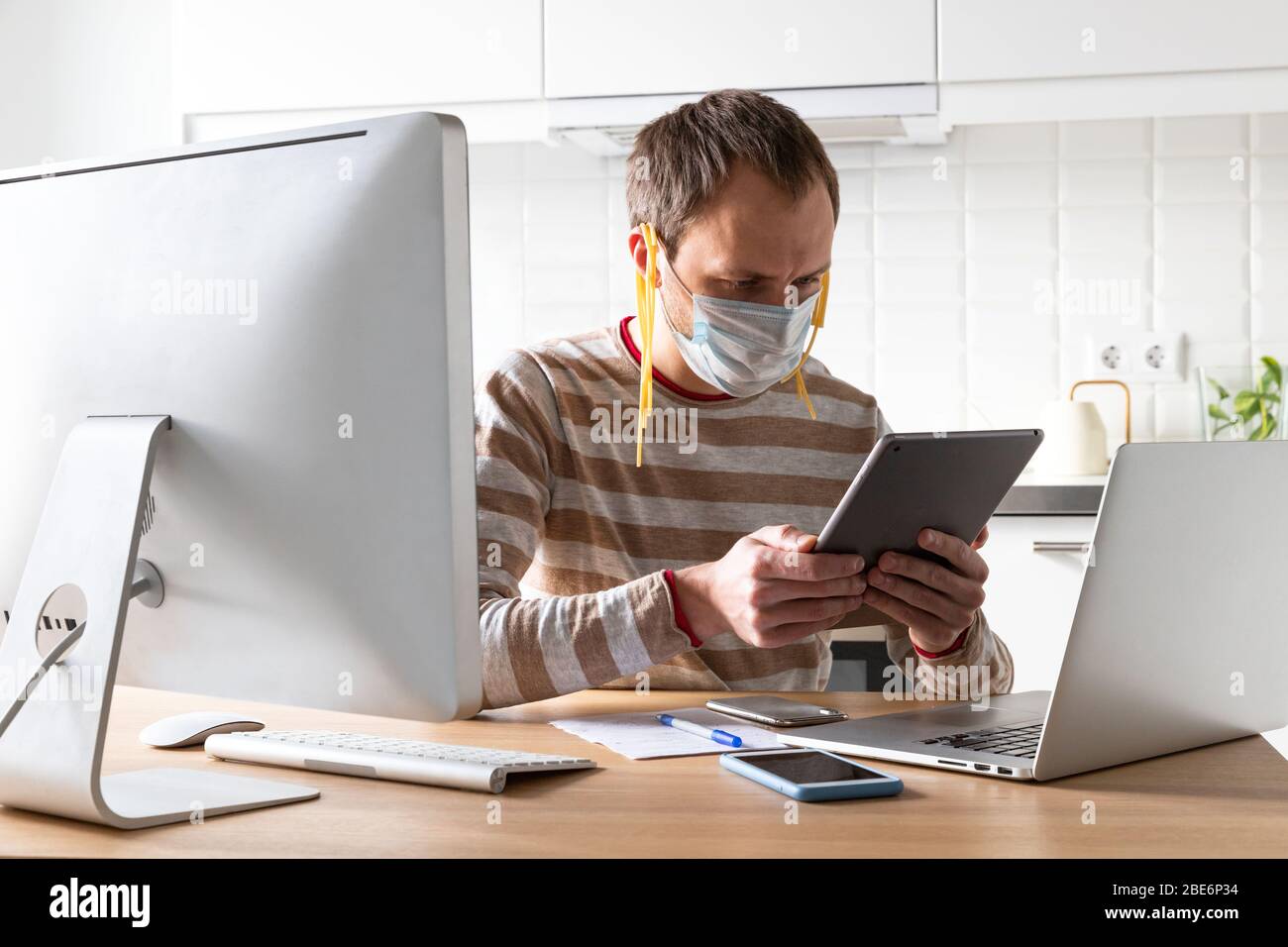 Man in face mask with noodles on his ears, reads fake/breaking news and a speech by the president on tablet about coronavirus during self-isolation, q Stock Photo