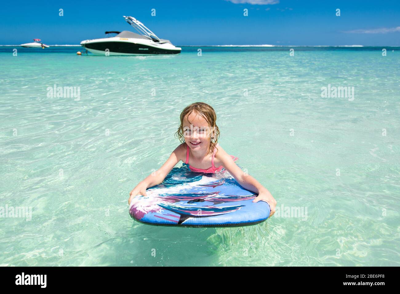 Little baby girl - young surfer with bodyboard has a fun on small ocean waves. Active family lifestyle Stock Photo