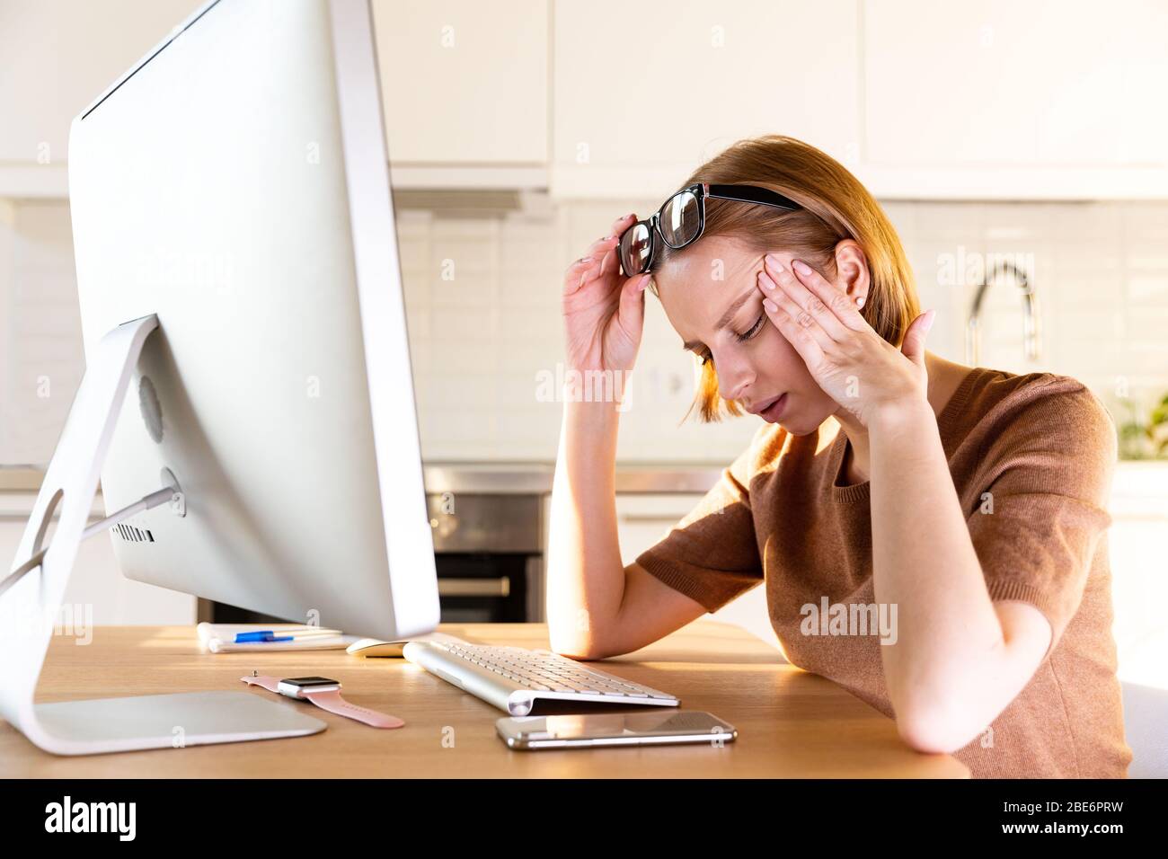 Tired woman freelancer has a headache, touching her temple after long work at computer during the period of self-isolation and remote work at home. Fa Stock Photo