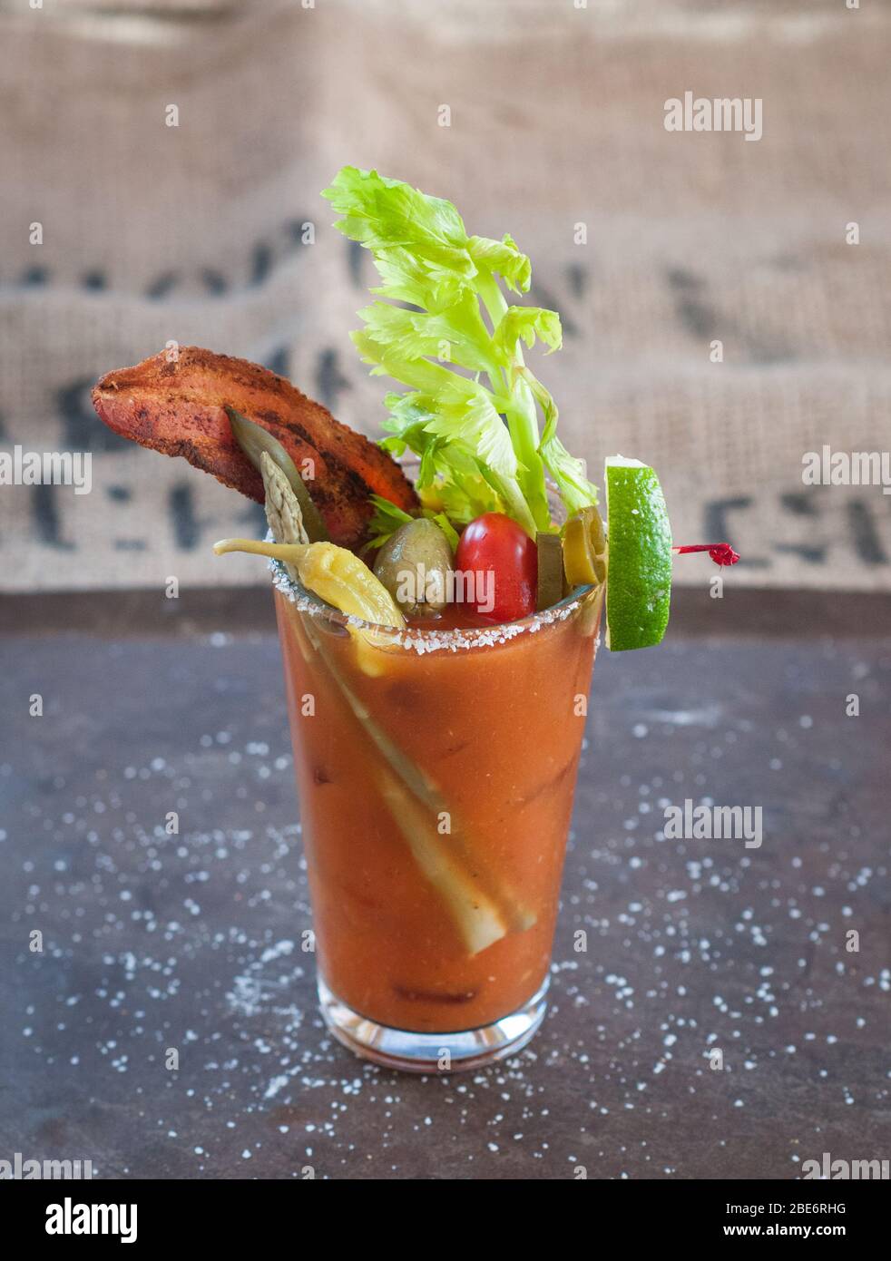 Single colorful Bloody Mary cocktail in a clear glass with a salted rim, bacon, celery, lime, asparagus garnishes. Stock Photo