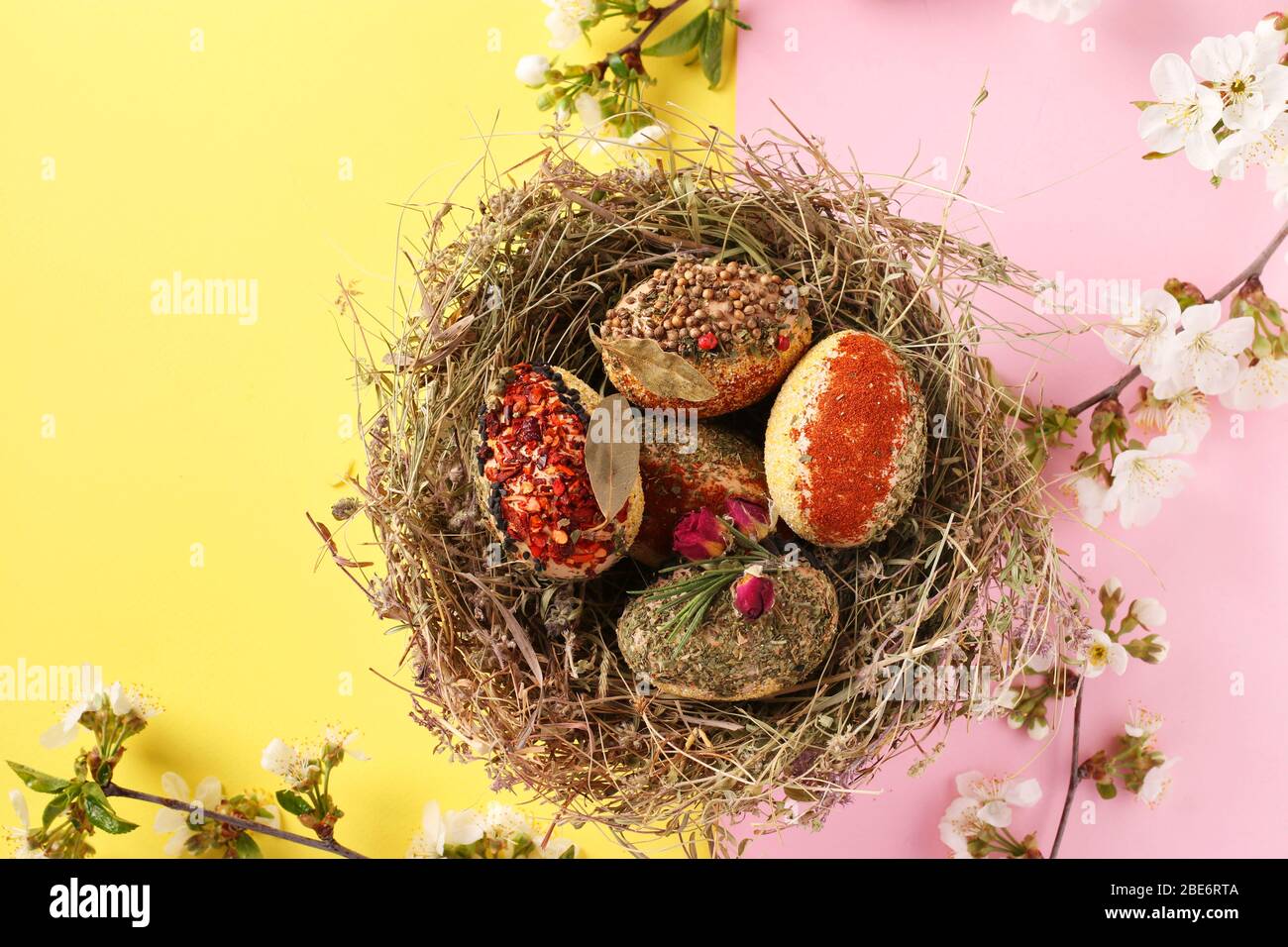 Easter eggs in a nest of herbs, decorated with various spices and cereal without dyes and preservatives on a pink and yellow background, Top view Stock Photo