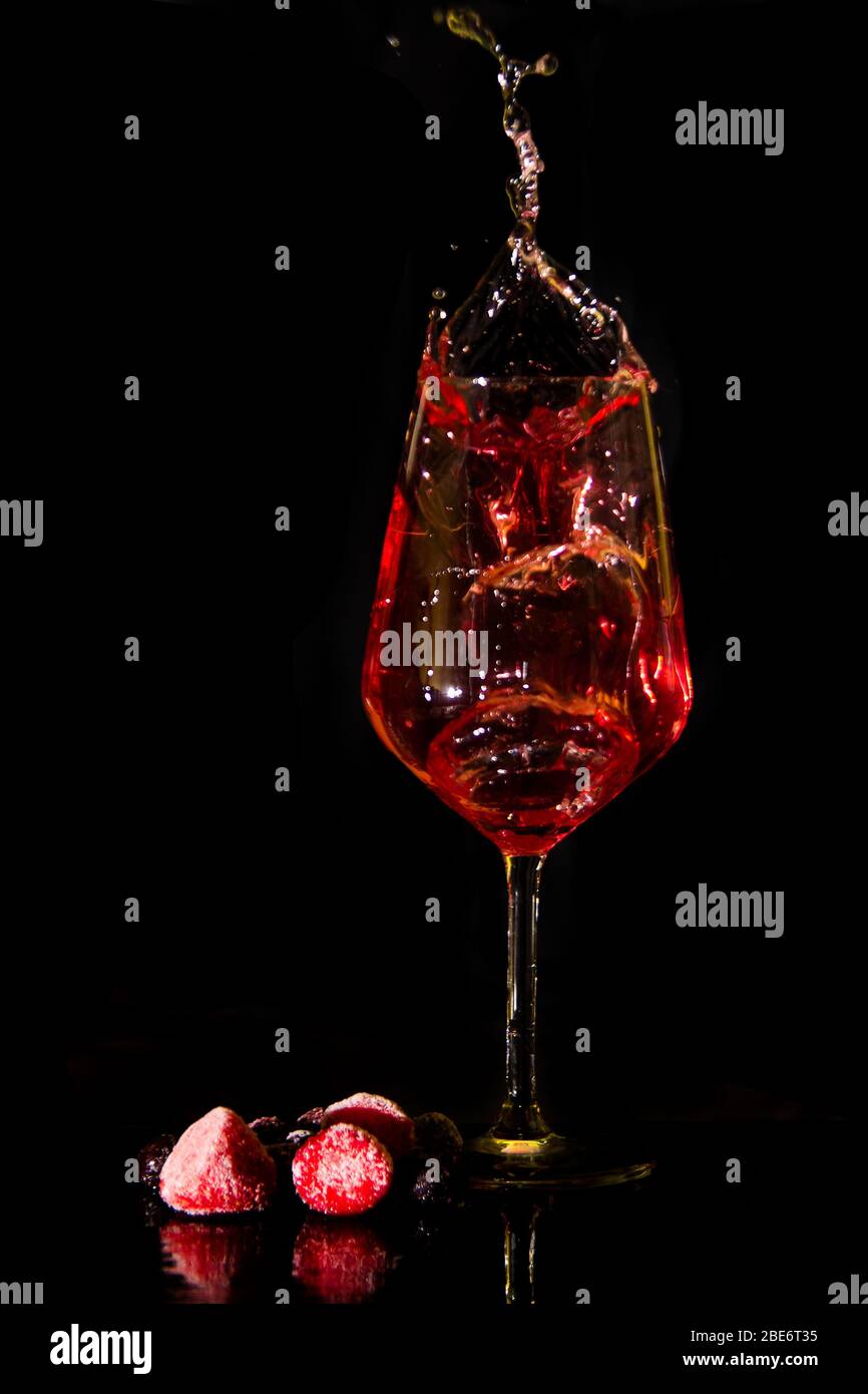 red or rose wine splashing from a wine glass against a black background with berries. Wine splash low key Stock Photo