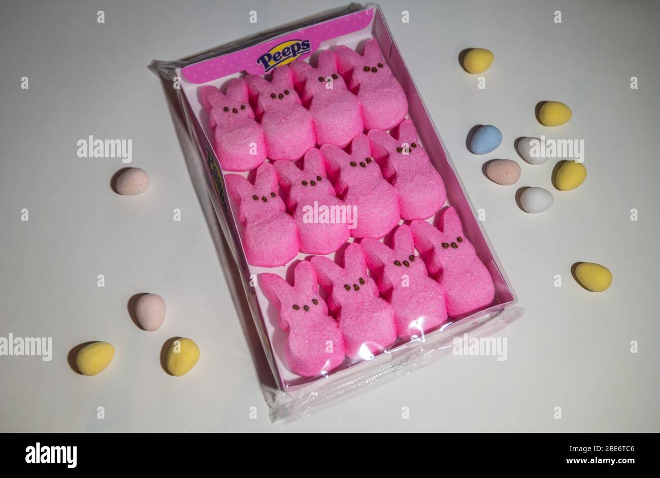 A unused package of Peeps pink Easter marshmallow bunnies on a white background with an assortment of colorful candy eggs surrounding Stock Photo