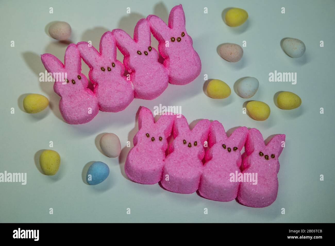 Arrangement of bright pink marshmallow bunny peeps with assortment of colorful candy eggs surrounding on a white background Stock Photo