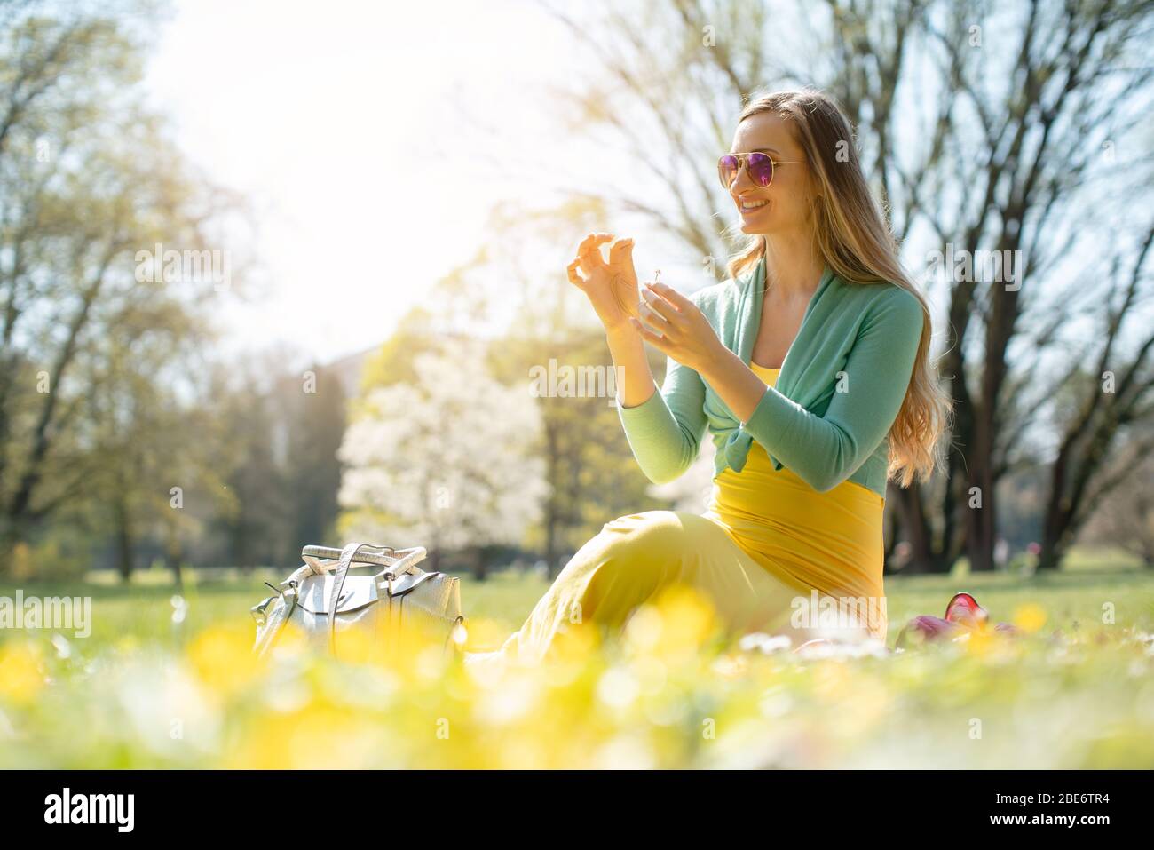Beautiful woman sitting on a spring meadow picking daisy flower Stock Photo