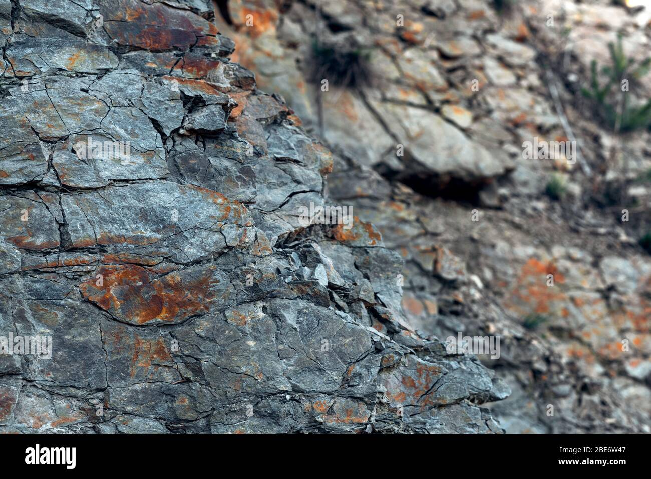 Natural basalt rock with cracks and crevices with a red color coming from iron. Rock wall texture. Graphite stone wall. Stone background. Stock Photo