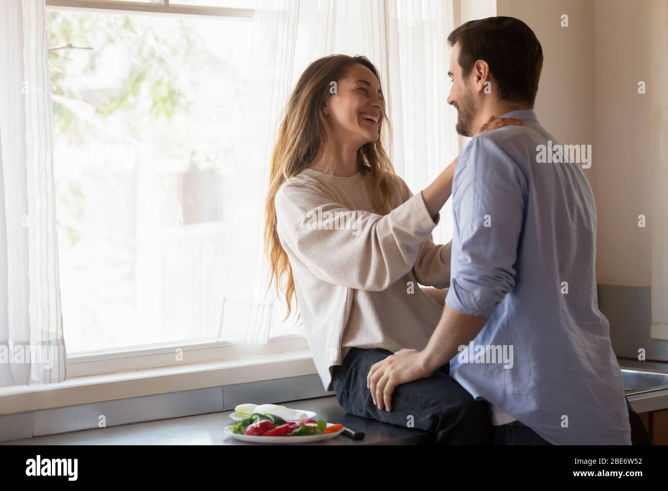 Smiling young lady sitting on countertop, chatting with husband. Stock Photo