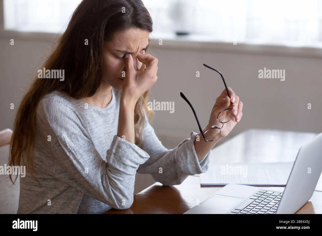 Exhausted young woman taking off glasses, suffer from eyes strain Stock