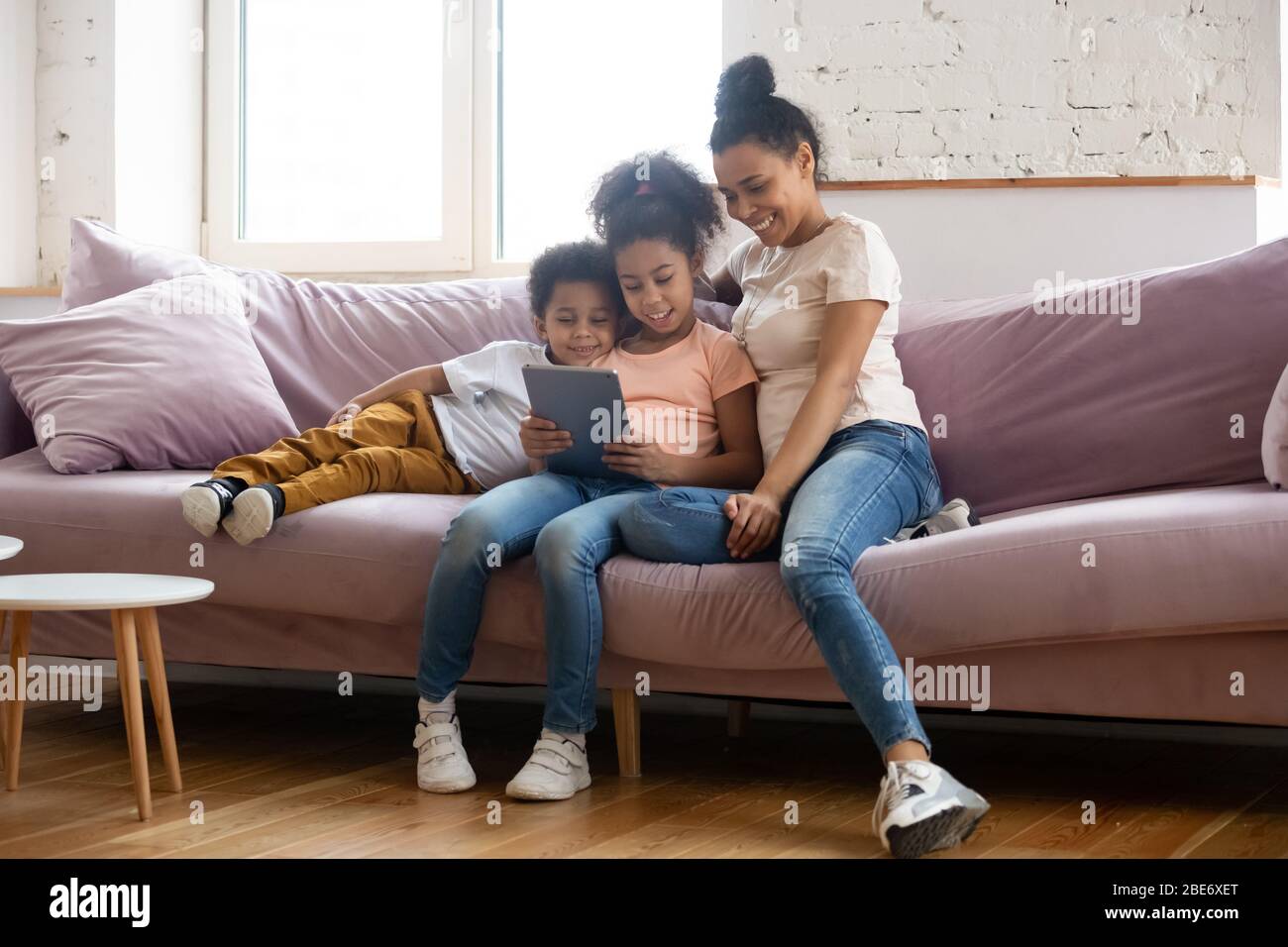 Happy african american mother looking at tablet screen with children. Stock Photo