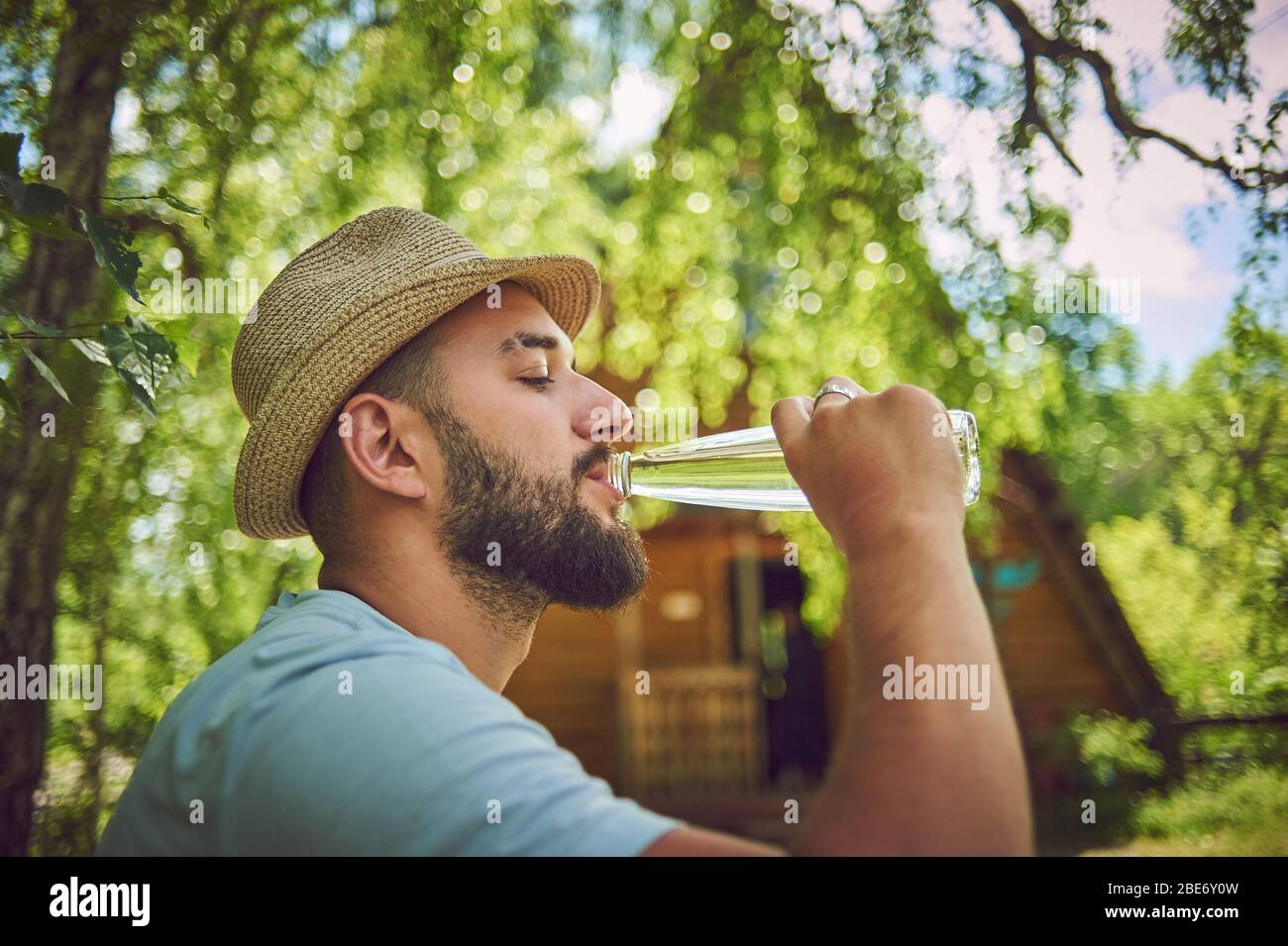 Portrait of a happy young man drinking some water from a bottle while sitting and resting in a park Stock Photo