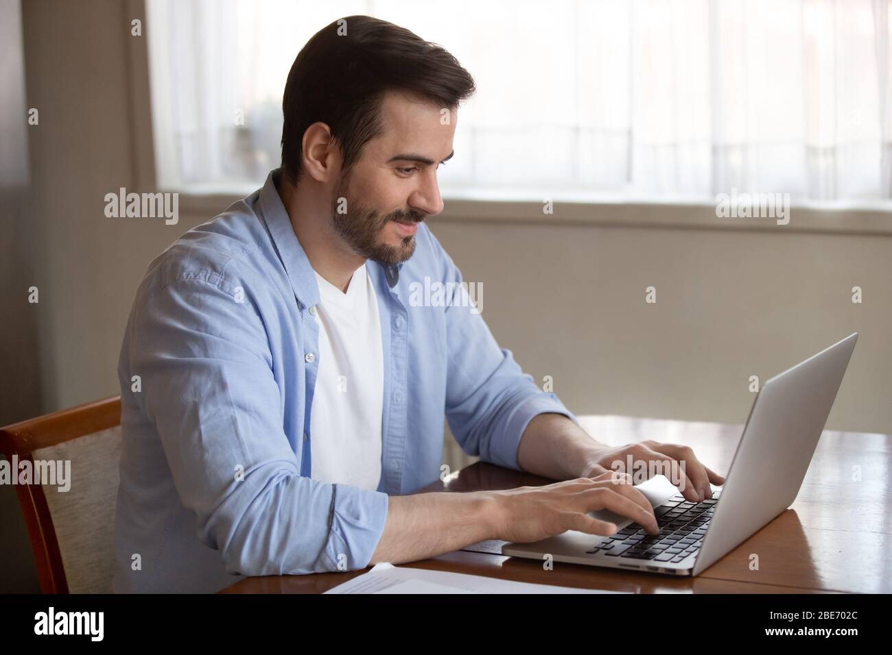 Handsome pleasant young man working remotely on computer at home. Stock Photo