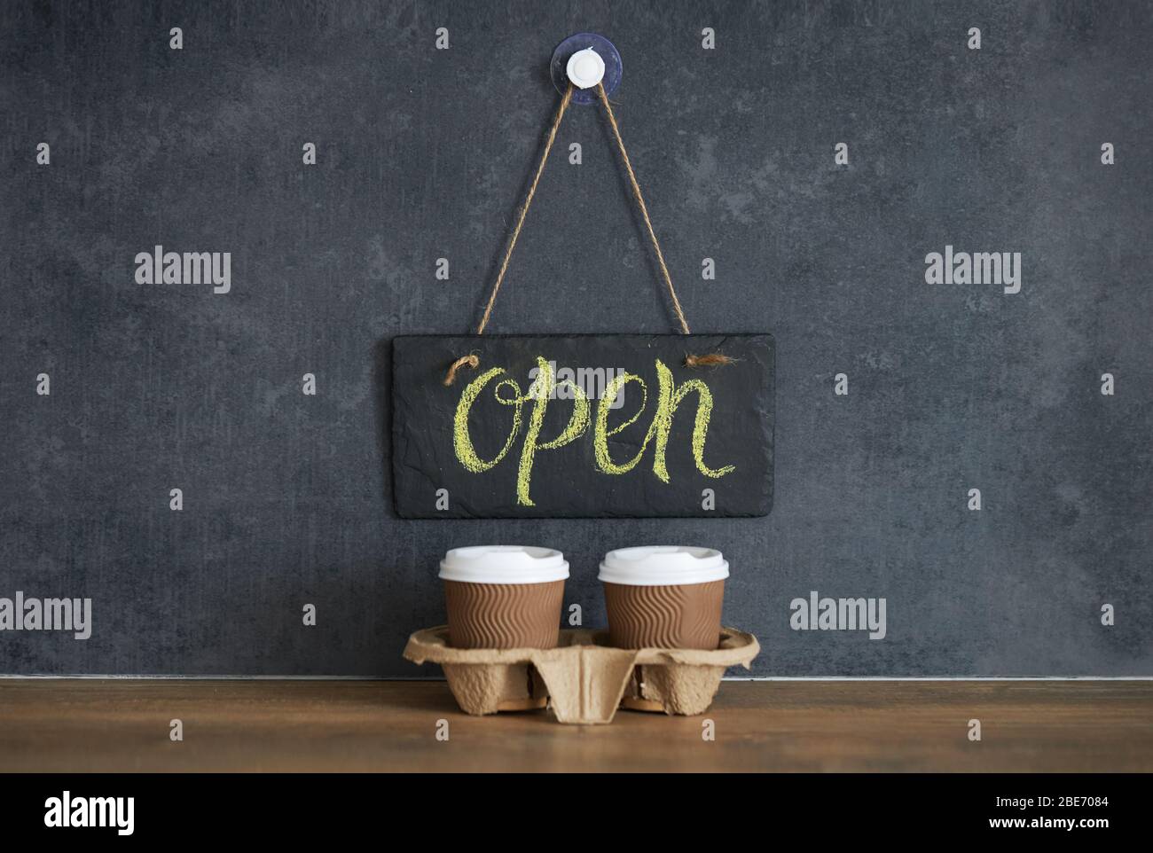 A sign that says Open on cafe, on a black chalk board. After quarantine. Takeaway coffee glasses on dark background. Business opening Stock Photo
