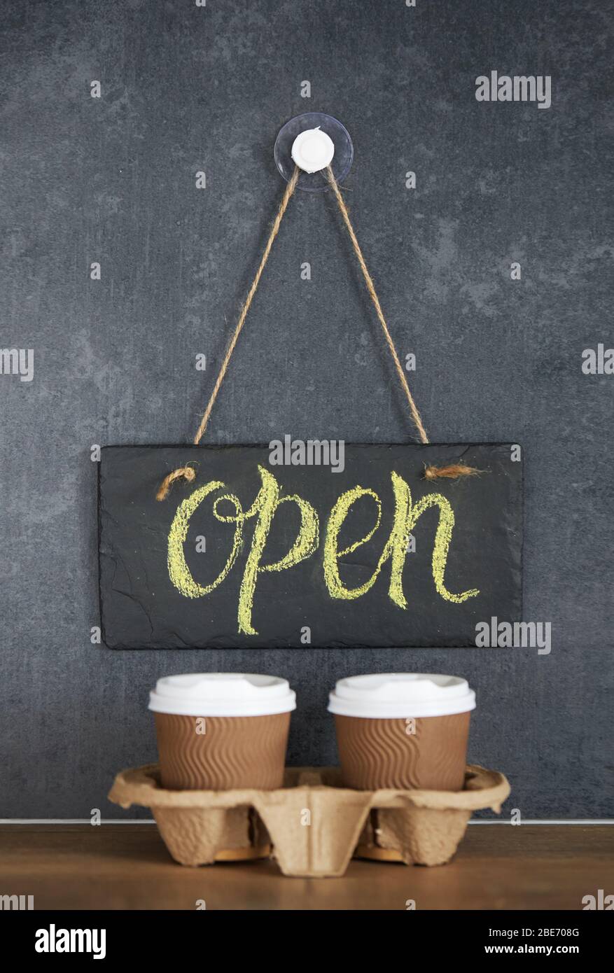 A sign that says Open on cafe, on a black chalk board. After quarantine. Takeaway coffee glasses on dark background. Business opening Stock Photo
