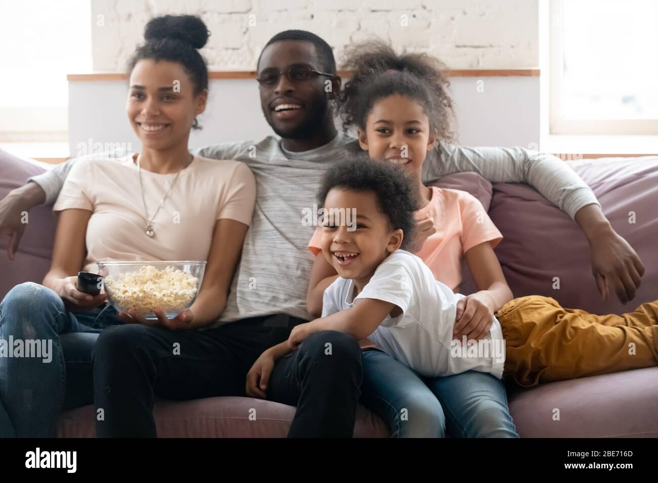 Happy african american family with kids watching funny tv show. Stock Photo