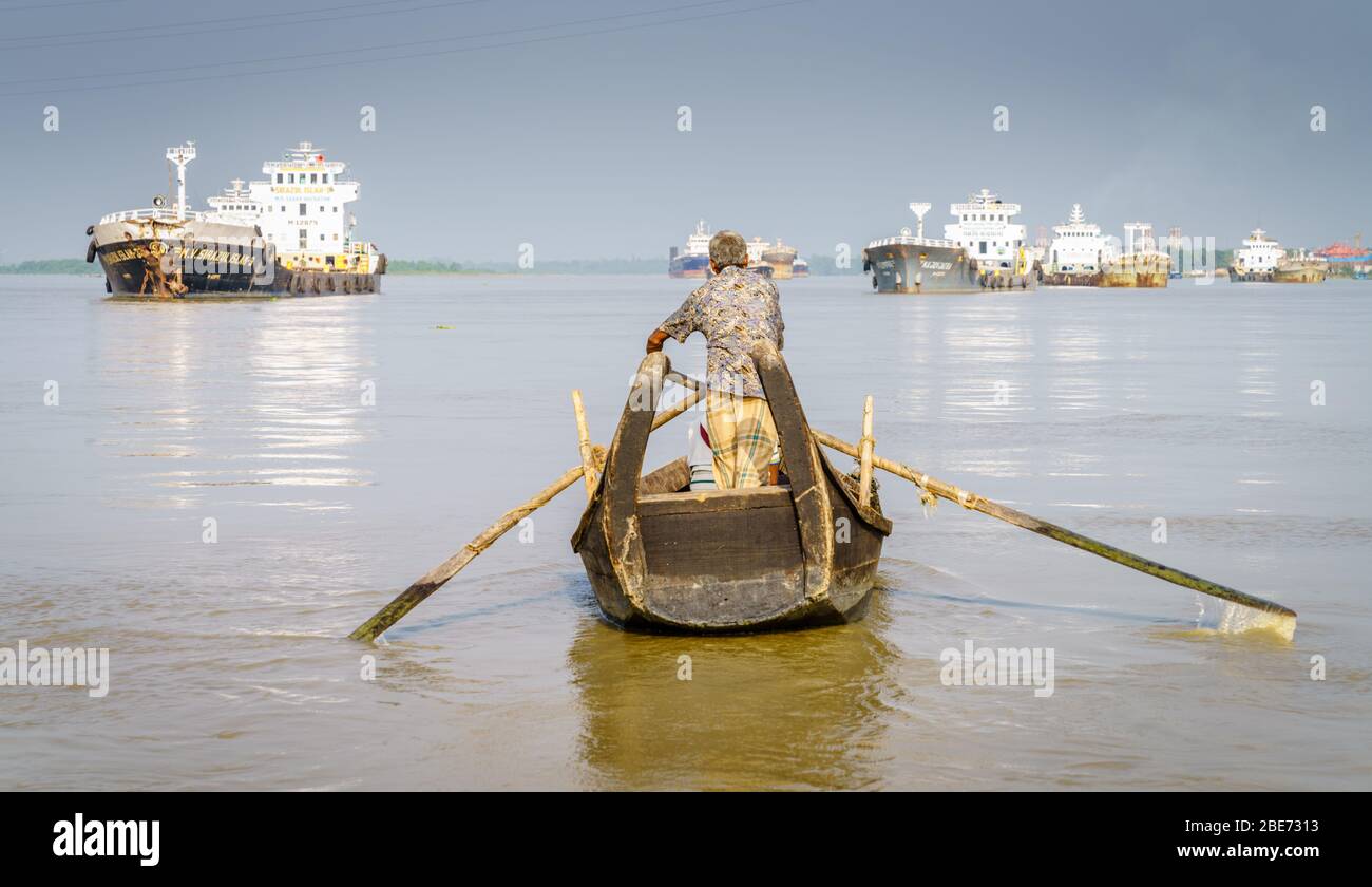 Chittagong, Bangladesh, December 22, 2017: Man is rowing a boat on the Karnaphuli River in Chittagong with fishing ships in the background Stock Photo
