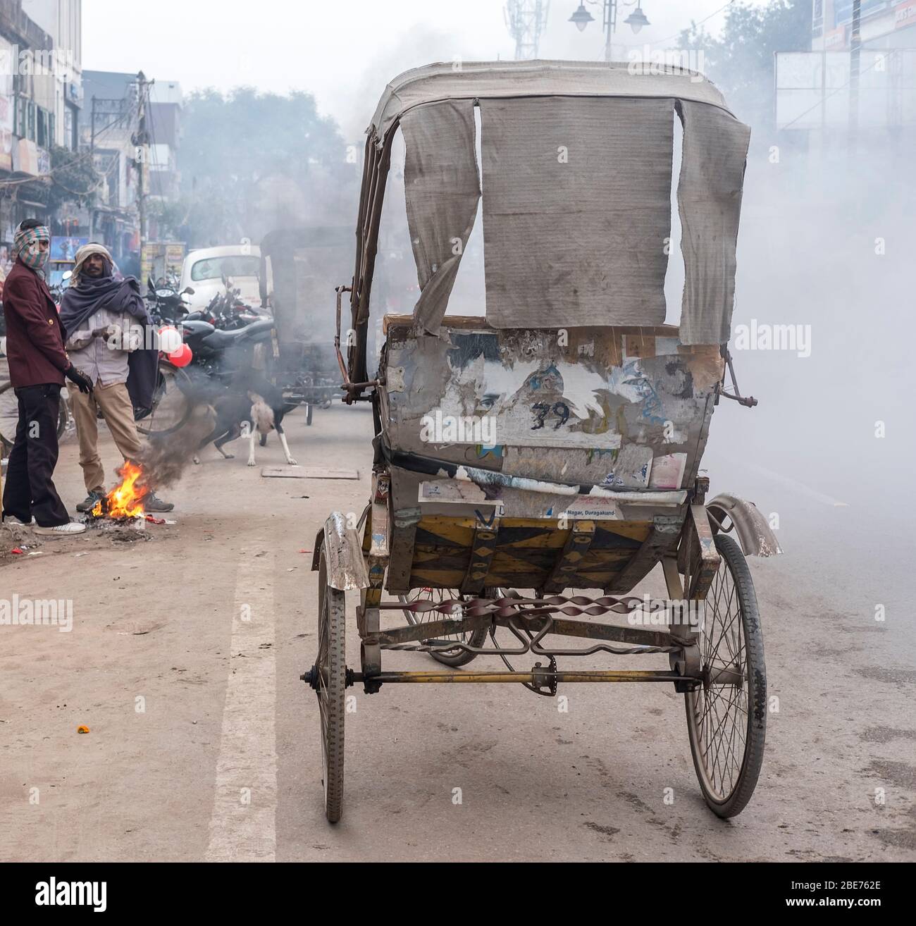 Old rickshaw parked on a street filled with toxic smoke from small fires made by locals to warm up during winter Stock Photo