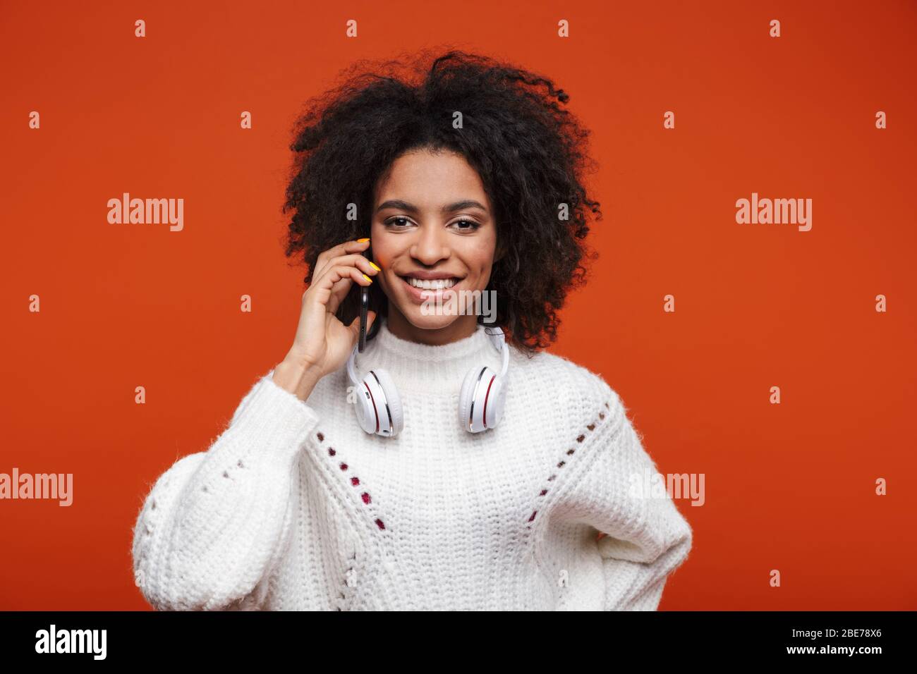Attractive young african woman wearing sweater talking on mobile phone isolated over red background Stock Photo