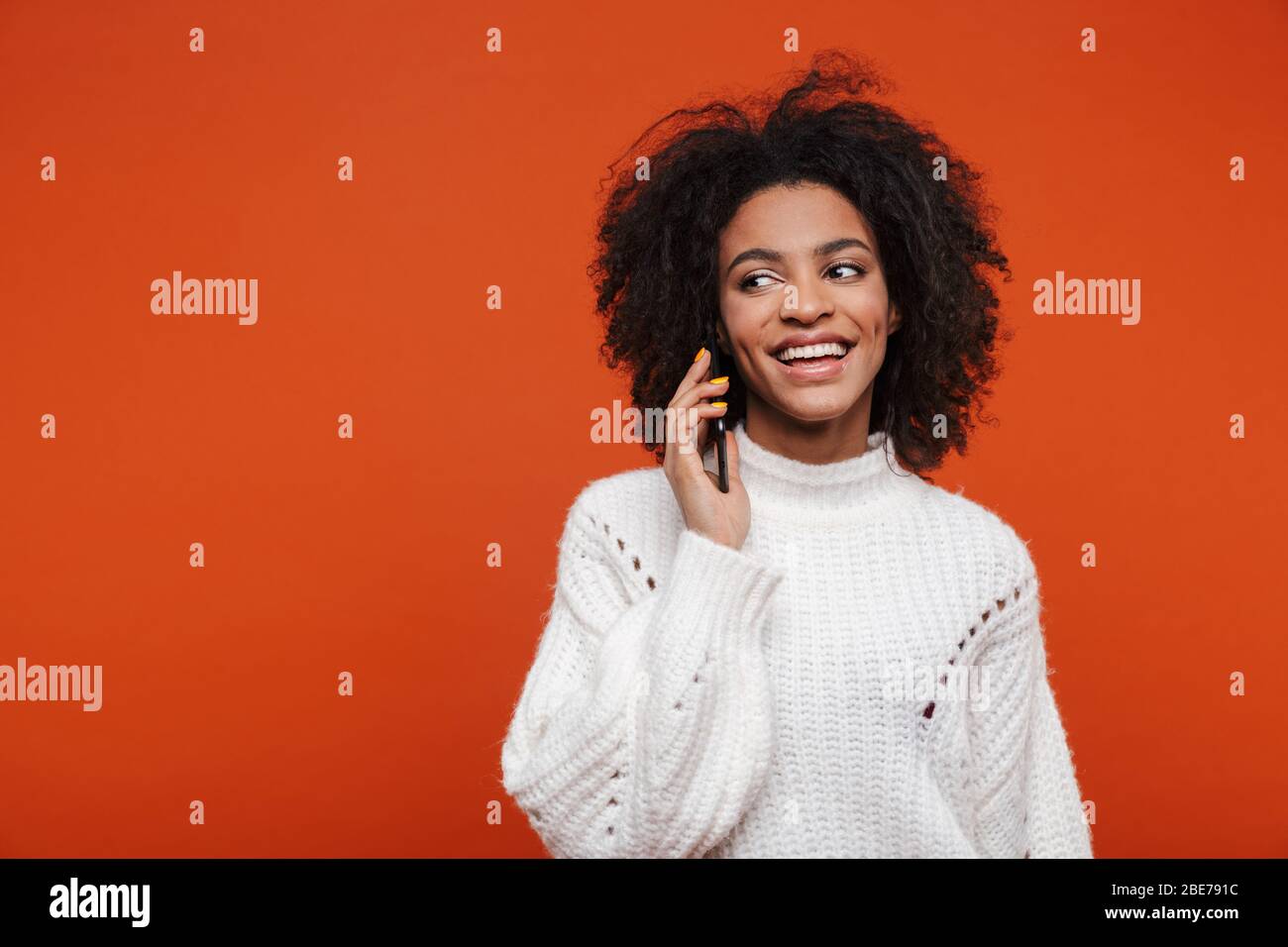 Attractive young african woman wearing sweater talking on mobile phone isolated over red background Stock Photo