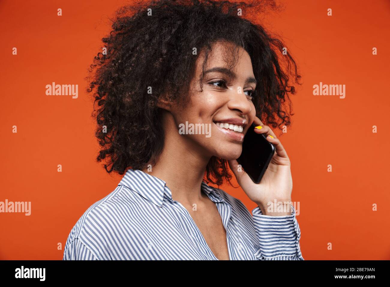 Smiling young attractive african woman talking on mobile phone isolated over red background Stock Photo