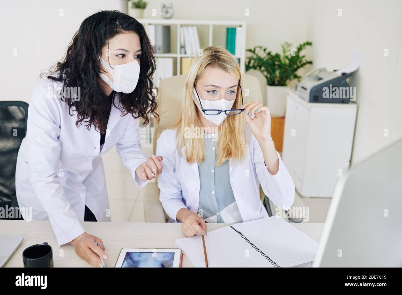 Young female medical workers in labcoats and medical masks analyzing chest x-ray on computer screen Stock Photo
