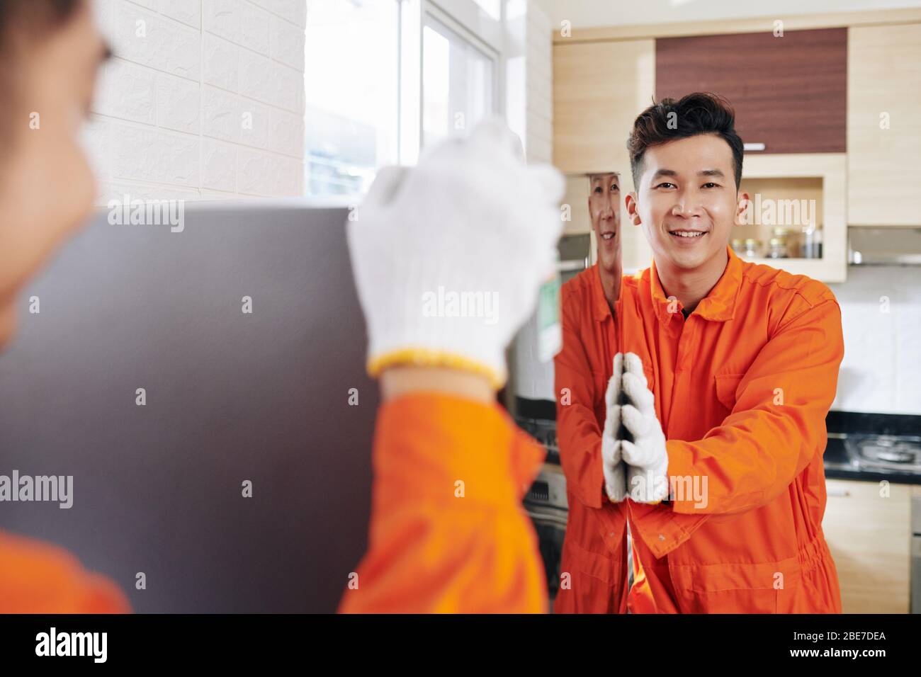 Smiling Vietnamese moving service workers transporting refrigerator in