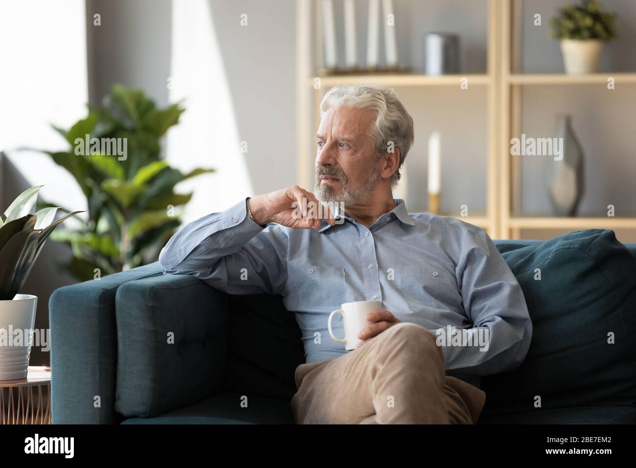 Thoughtful older man sitting on couch alone, feeling lonely Stock Photo