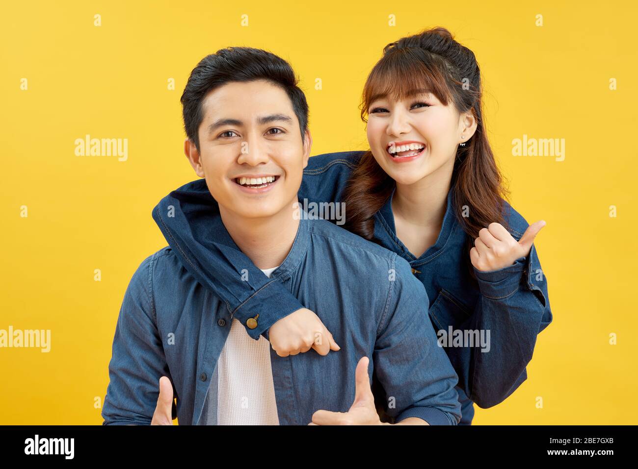Portrait of smiling couple man and woman showing thumb up together while doing piggyback ride isolated over yellow background Stock Photo