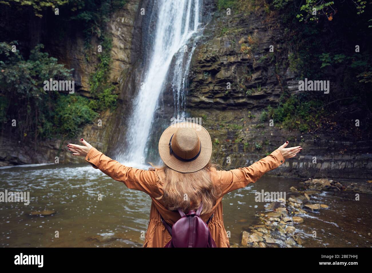 Woman in Hat rise her hand near waterfall in Botanical Garden in Tbilisi, Georgia Stock Photo