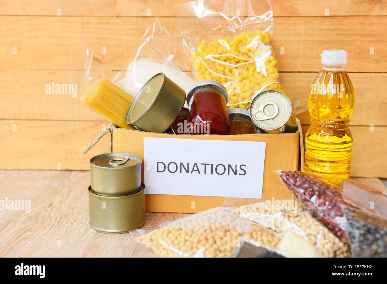 Donations box with canned food on wooden table background / pasta