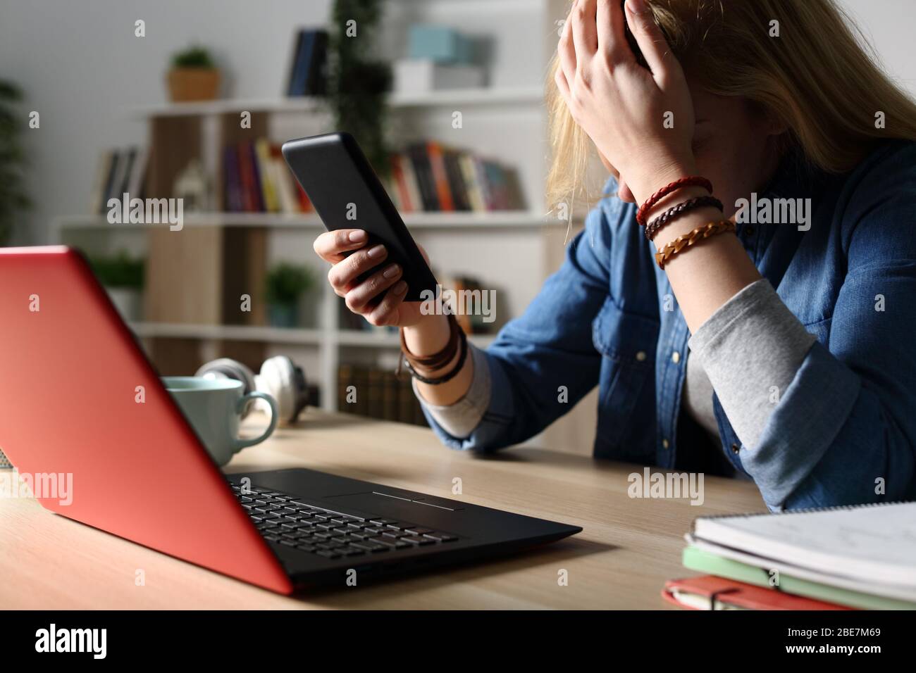 Close up of sad student reading bad news on smart phone sitting on a desk at home at night Stock Photo