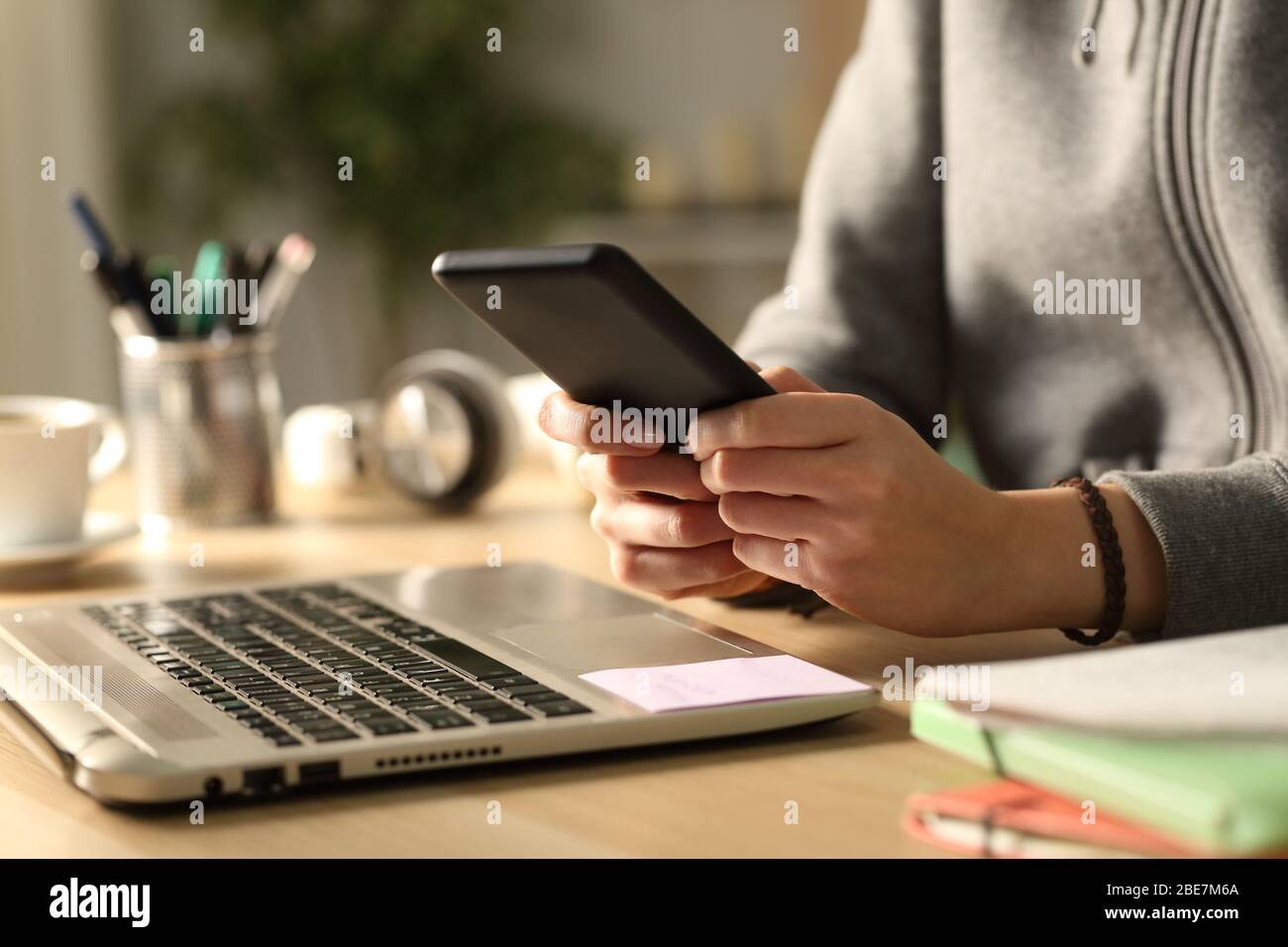 Close up of student girl hands typing on smart phone sitting on a desk at home at night Stock Photo