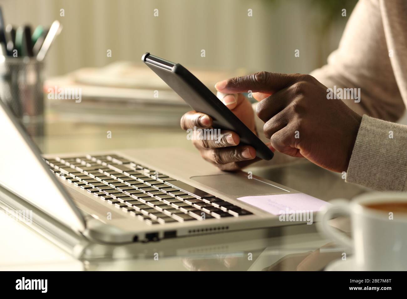 Close up of black man hands using smart phone with laptop at home Stock Photo