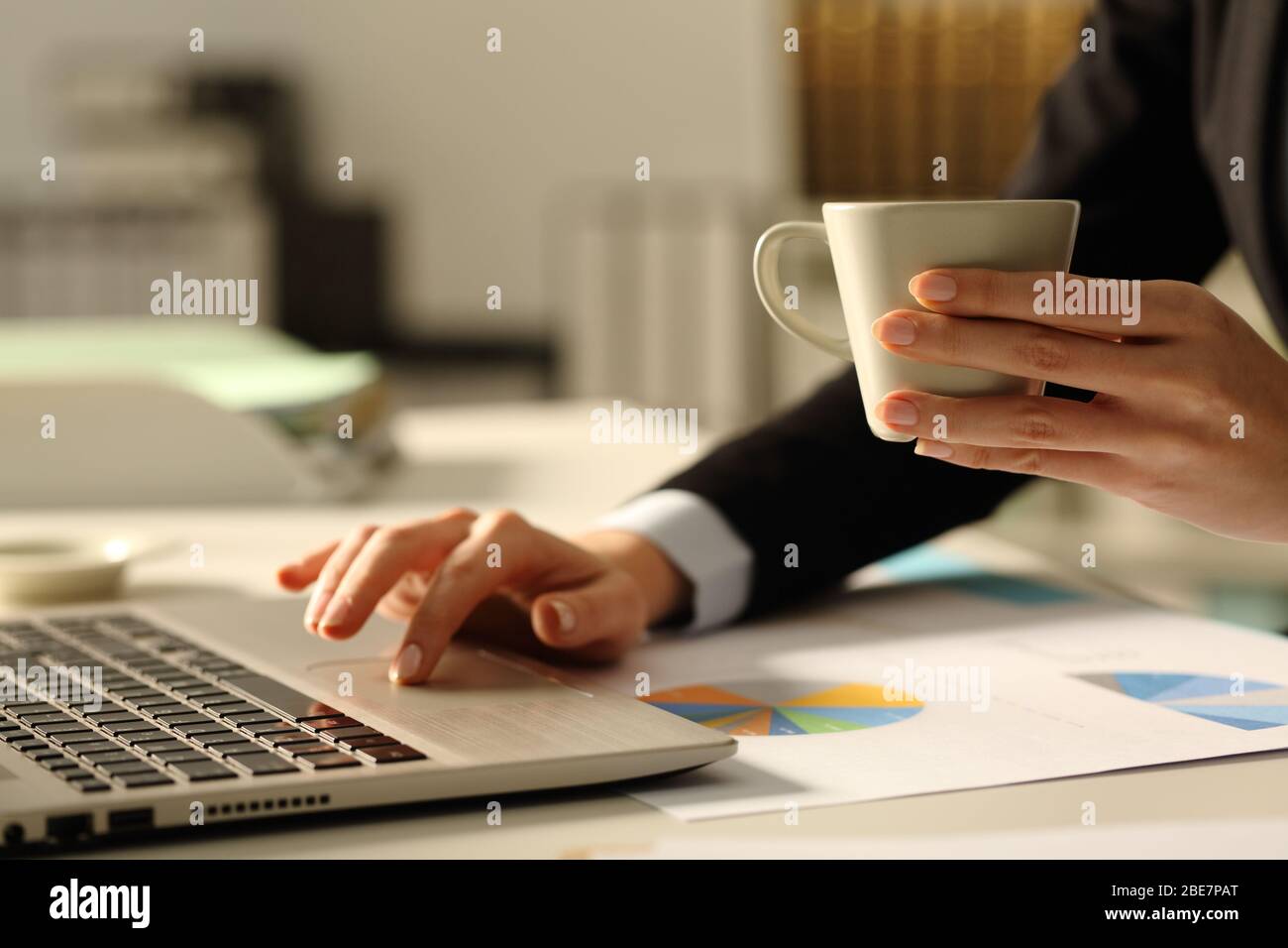 Close up of executive woman hands using laptop holding coffee cup in the office at night Stock Photo