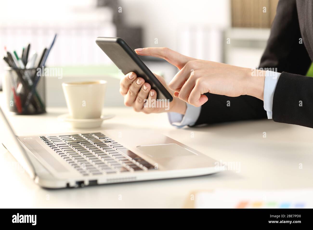 Close up of executive woman hands with laptop checking smart phone at the office Stock Photo