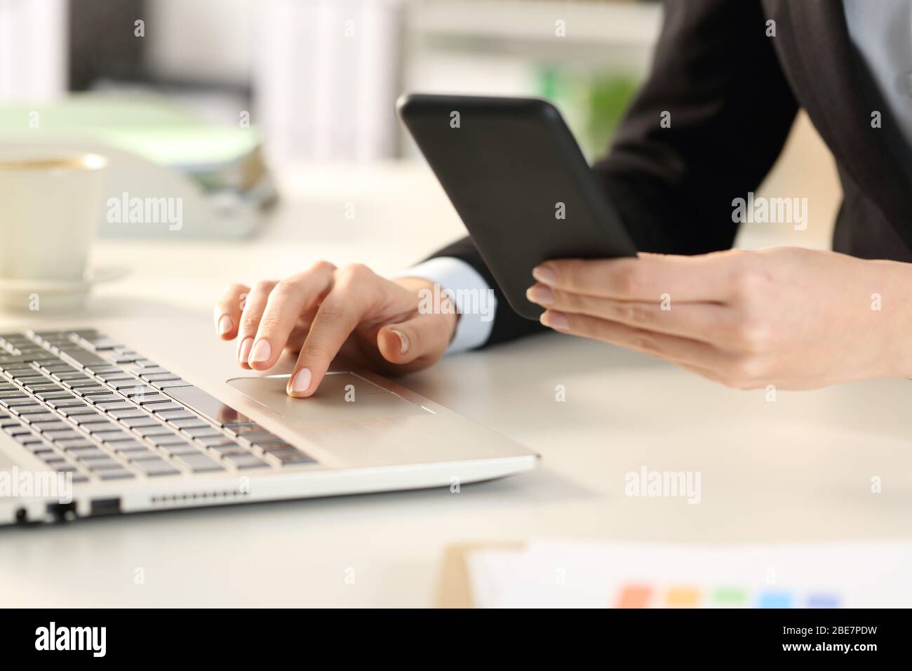Close up of executive woman hands using mobile phone and laptop on a desk at office Stock Photo