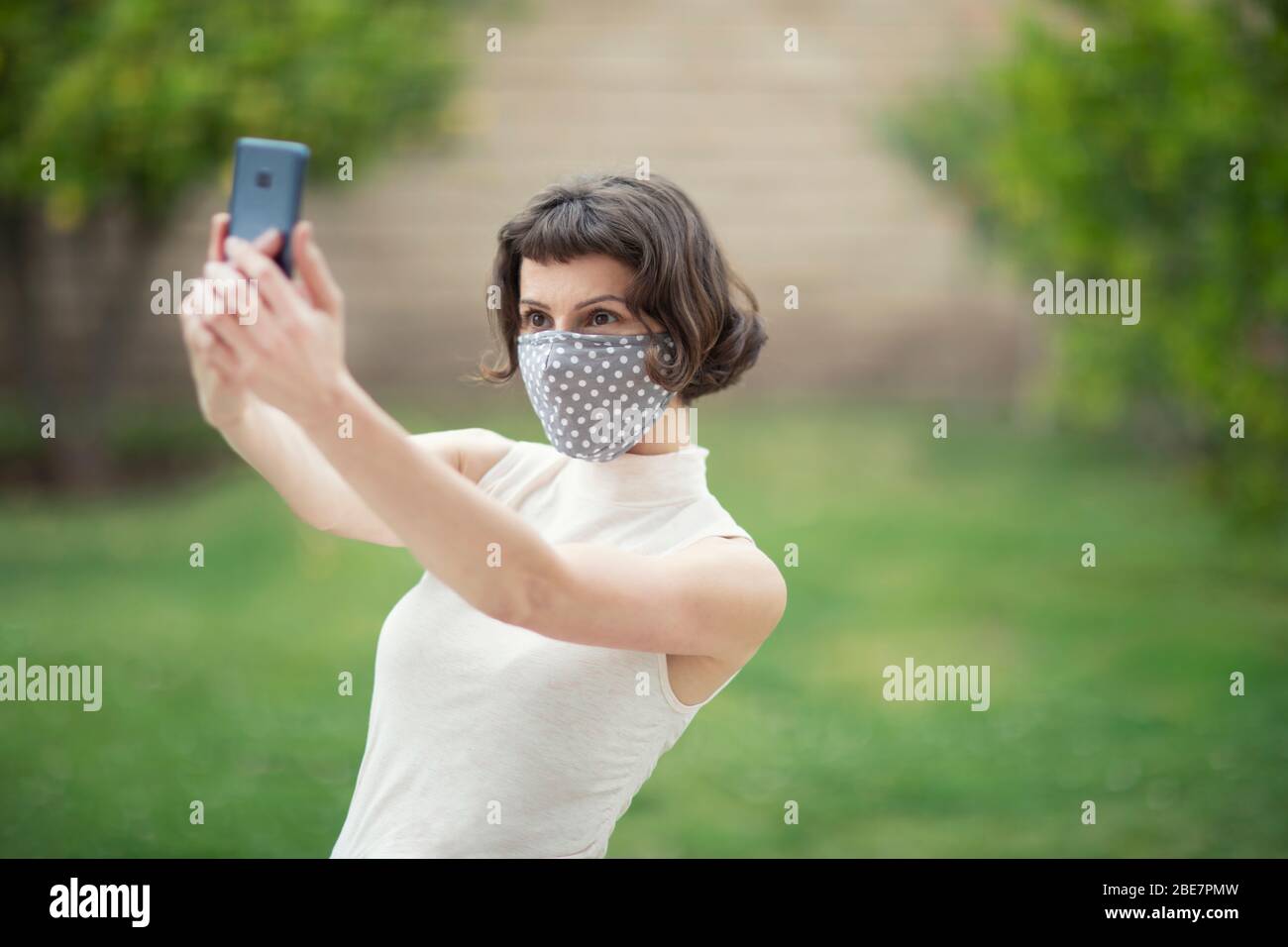 A white woman in a fabric face mask while using her phone for selfie