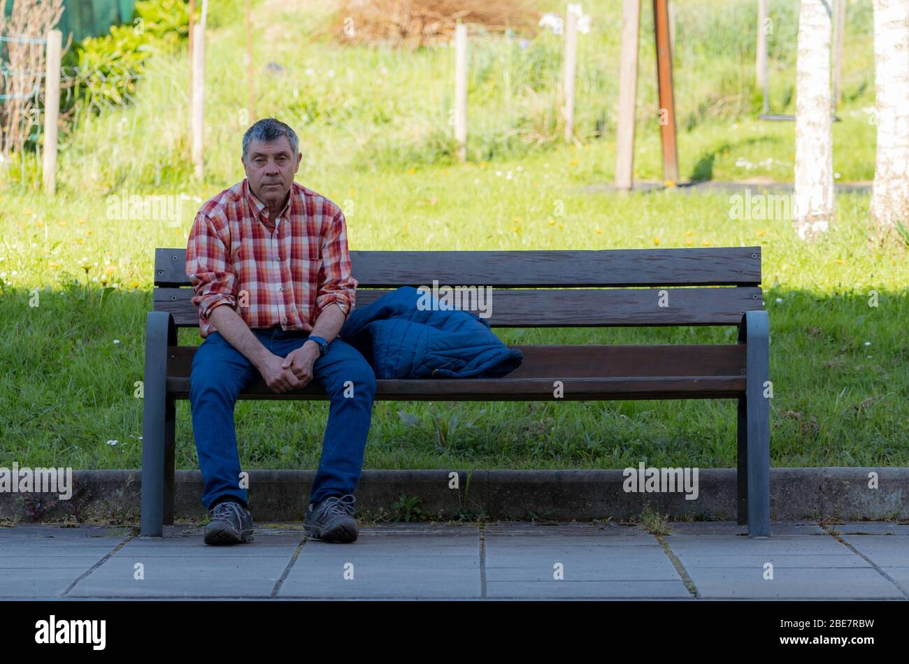 Gipuzkoa, SPAIN-MARCH 22, 2018 : Sad and tired man sitting on wooden bench in park. Old man wear plaid shirt and jeans. Caucasian senior man sitting Stock Photo