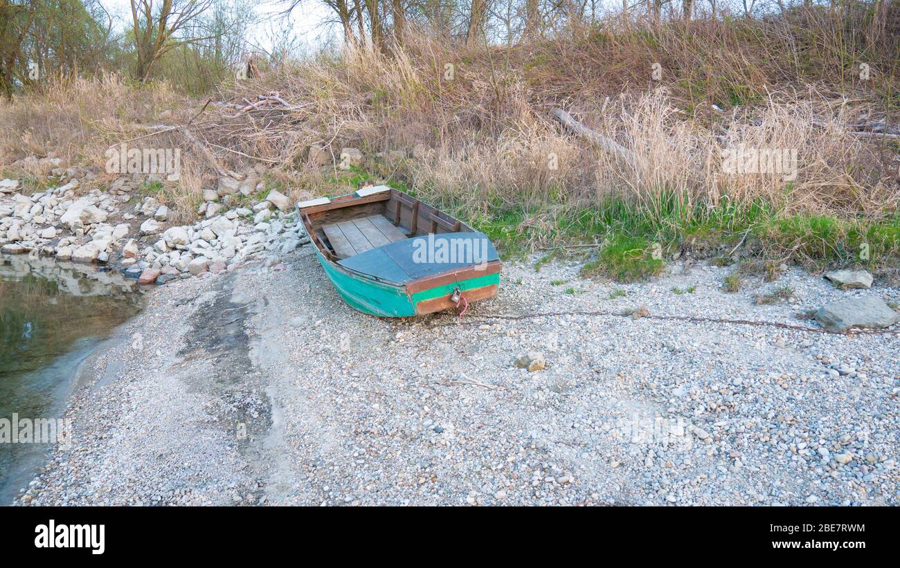 An old wooden fishing boat remained on the shore of the lake. An abandoned fishing boat on the bank of the Danube. A green boat left on a pebble bank. Stock Photo