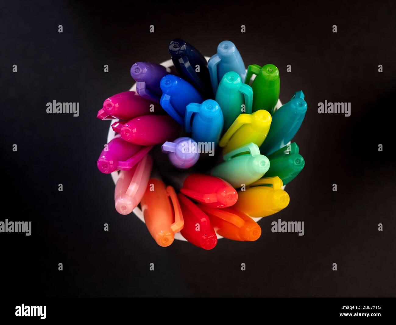 Top down view of colouring pens spiralling in a pot against a black background Stock Photo