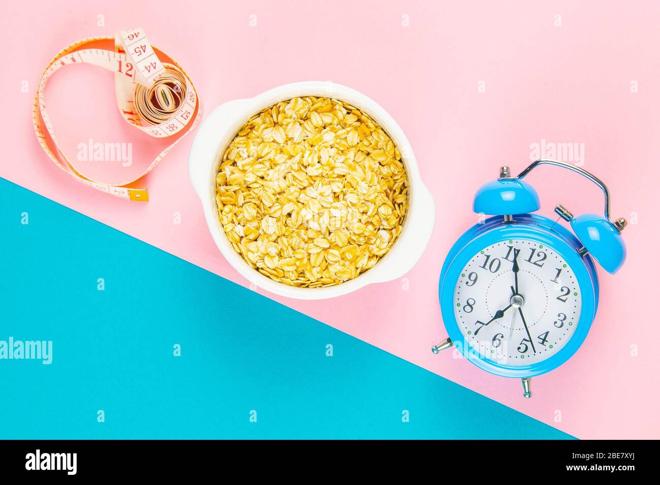 Blue alarm clock with oatmeal and measuring tape on a pink and blue