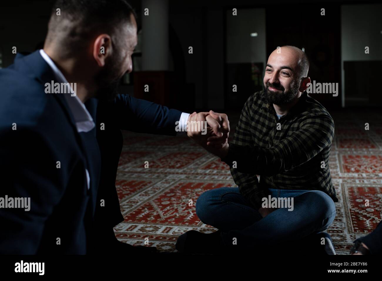 Group of Muslims Sitting on Carpet Afther Praying in the Mosque and Making Handshake Stock Photo