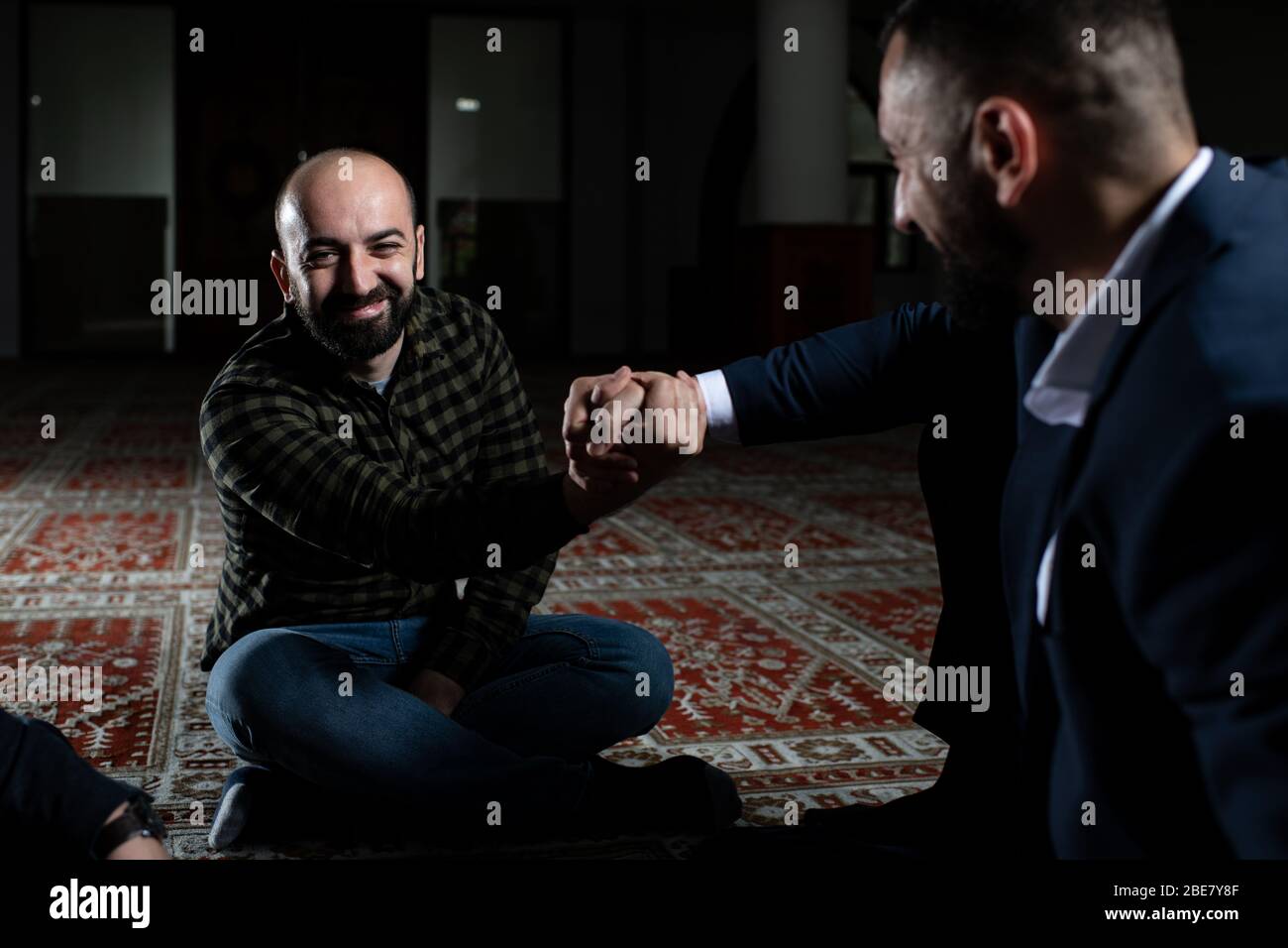 Group of Muslims Sitting on Carpet Afther Praying in the Mosque and Making Handshake Stock Photo