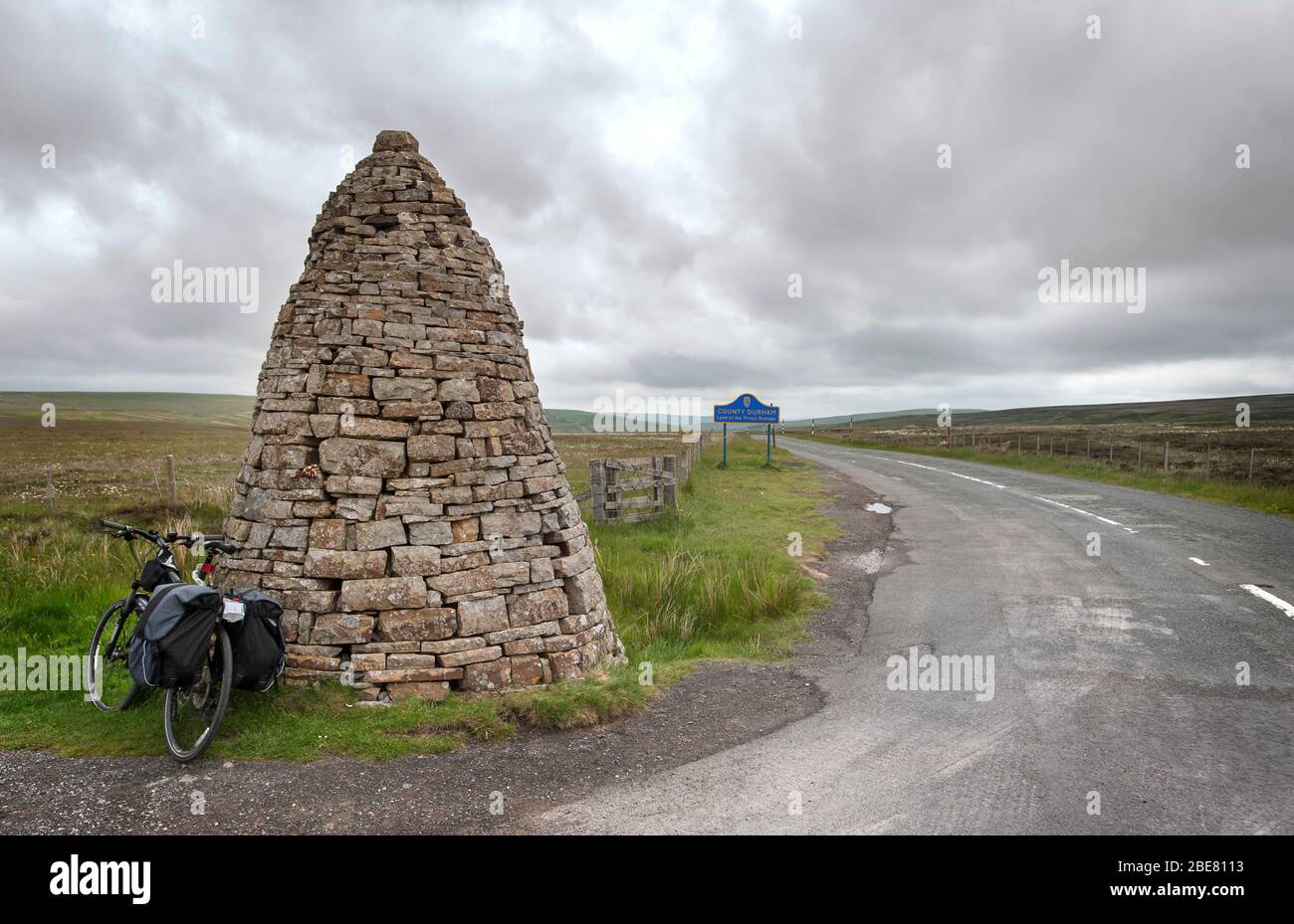 Touring bike leans against a large stone cairn, or currick, at Shorngate Cross on the border of Northumberland and County Durham, UK Stock Photo