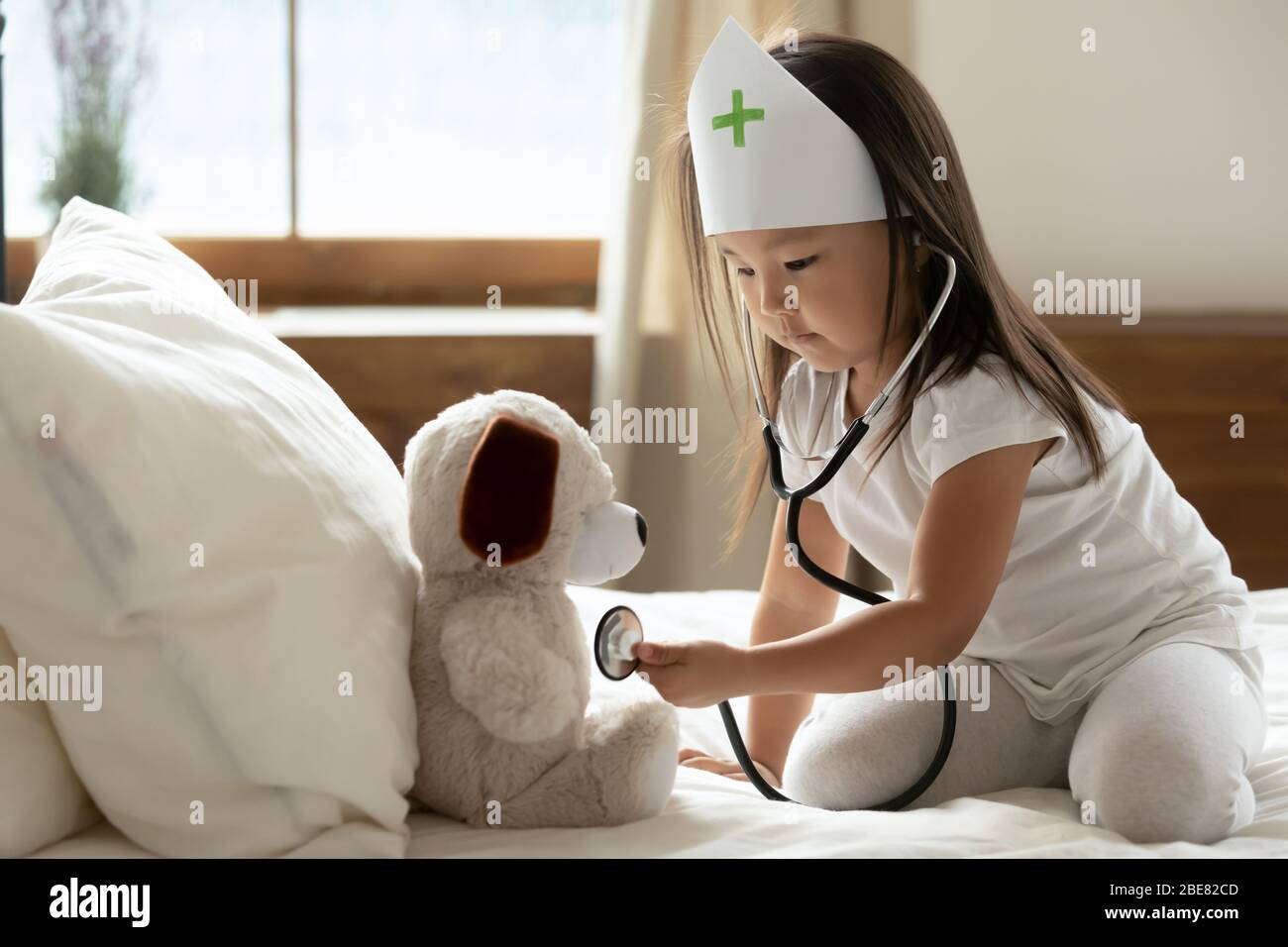 Asian little girl hold phonendoscope listens heartbeat to stuffed toy Stock Photo