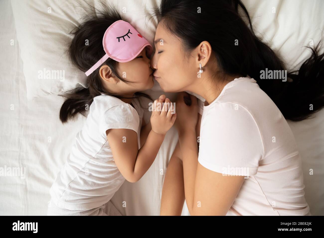 Asian mom kisses little daughter before bedtime sleeping above view Stock Photo