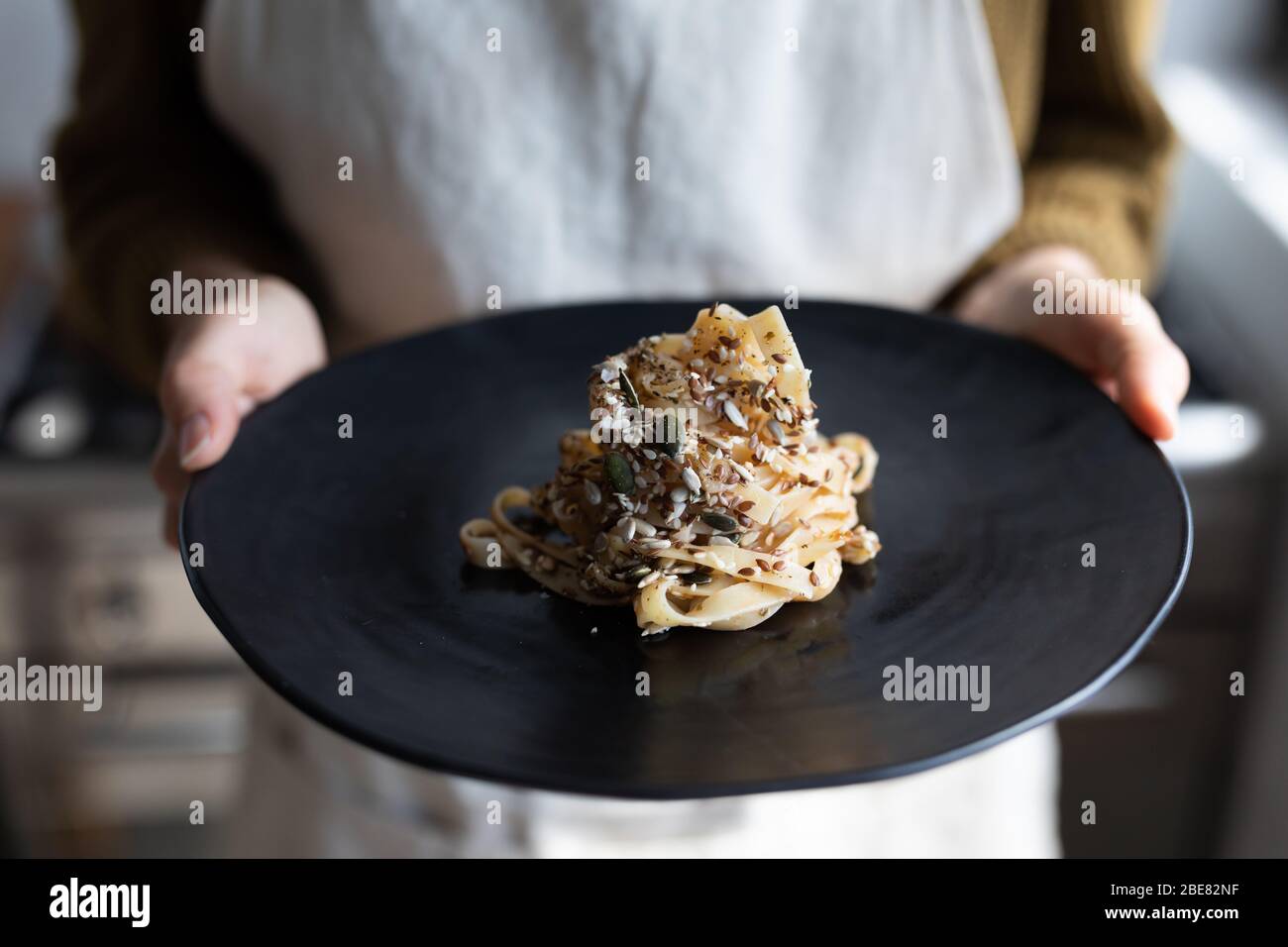 Mid section of Caucasian woman wearing an apron and  presenting plate of pasta Stock Photo