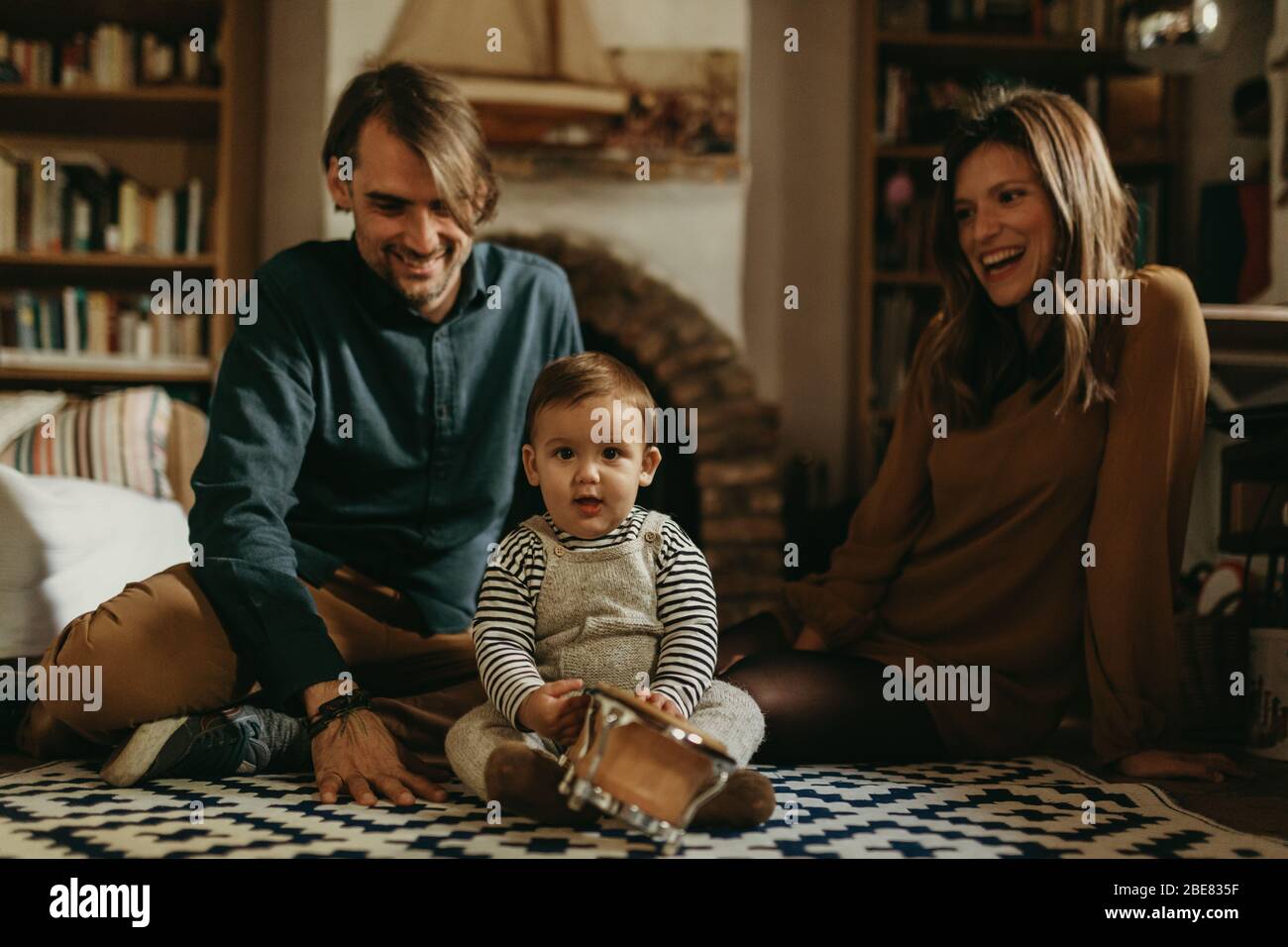 Young happy couple staying at home with their baby son sitting on the living room floor. Stock Photo