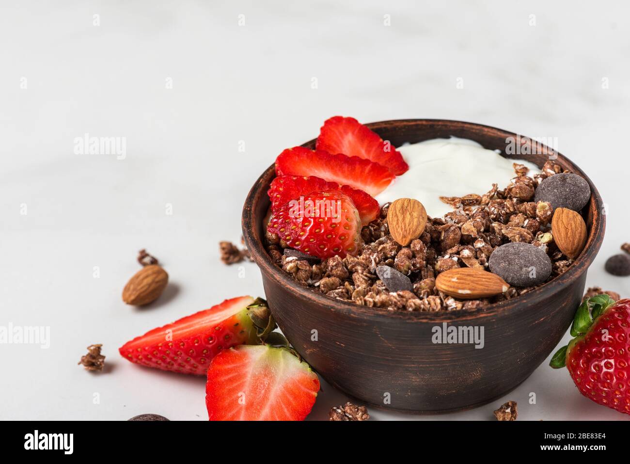 Healthy diet breakfast. bowl of oat chocolate granola with yogurt, fresh strawberries and almonds on white marble table. close up Stock Photo