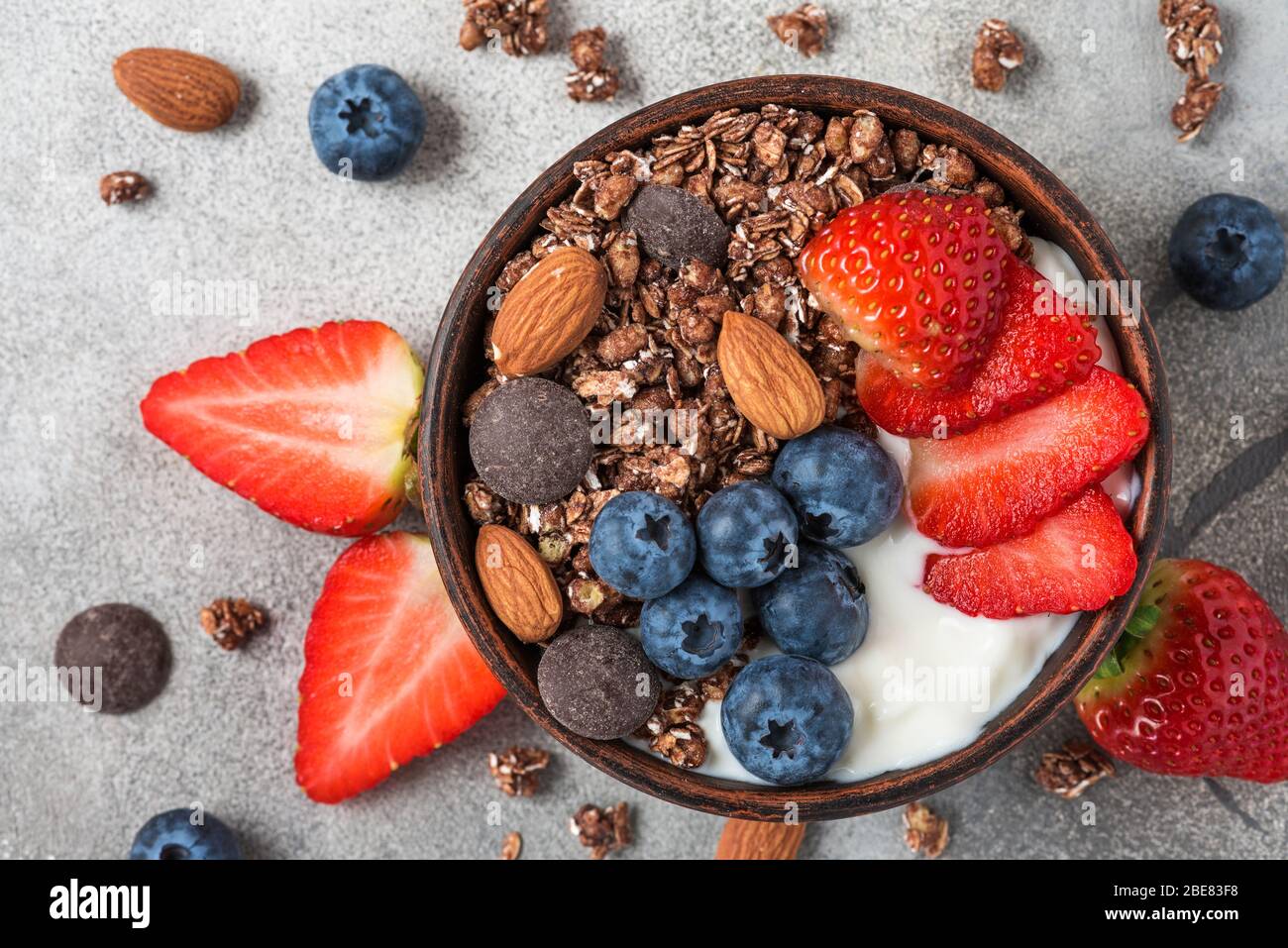 Healthy diet breakfast. bowl of oat chocolate granola with yogurt, fresh berries and almonds on gray table. top view Stock Photo