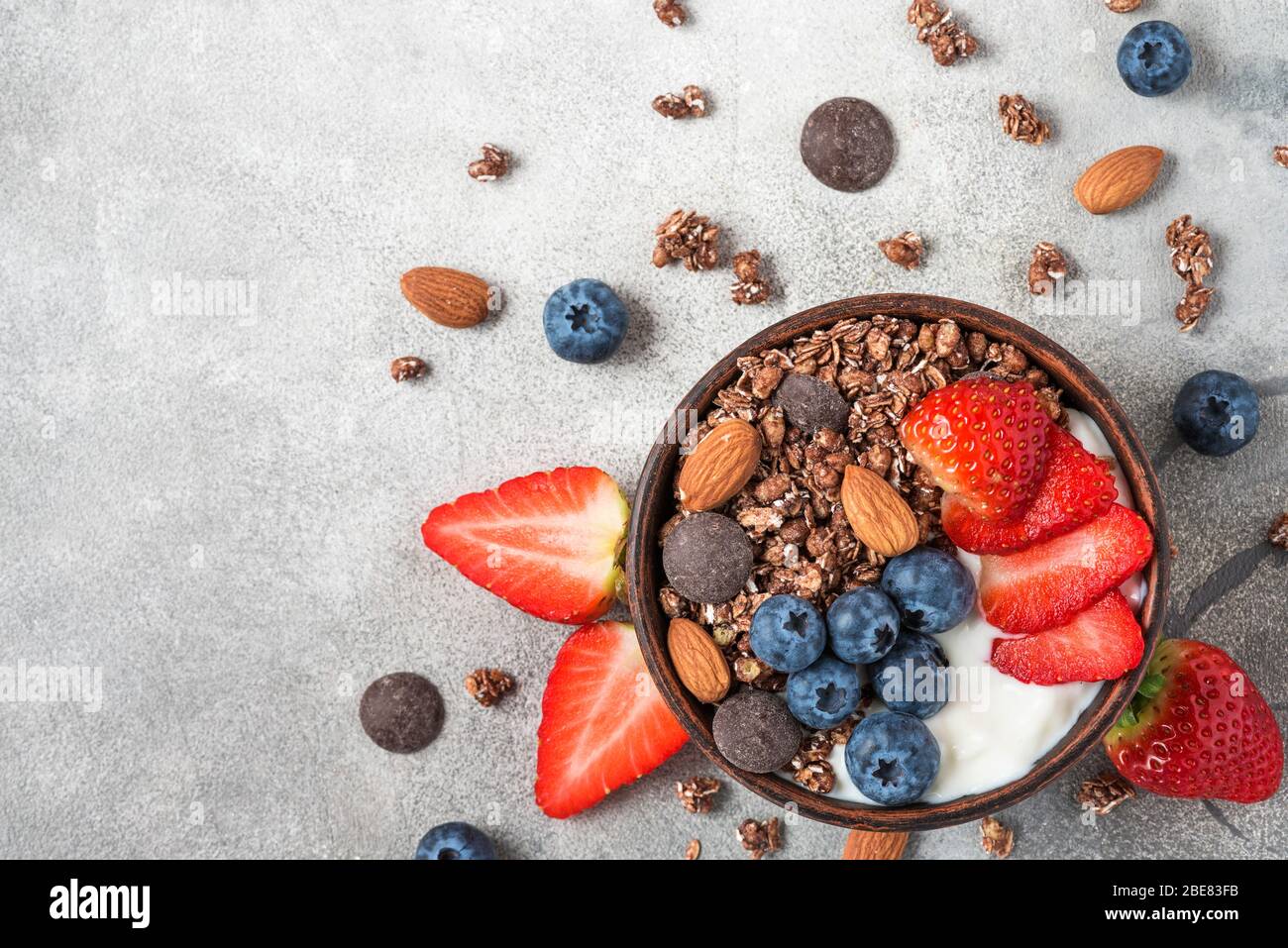 yogurt with oat chocolate granola, fresh berries and nuts in a bowl on gray background for healthy breakfast. top view with copy space Stock Photo